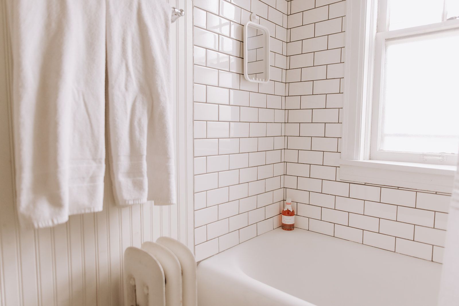 Clean and vintage bathroom with nearly all white accents. The only color is a bottle of pink bath wash in the corner.
