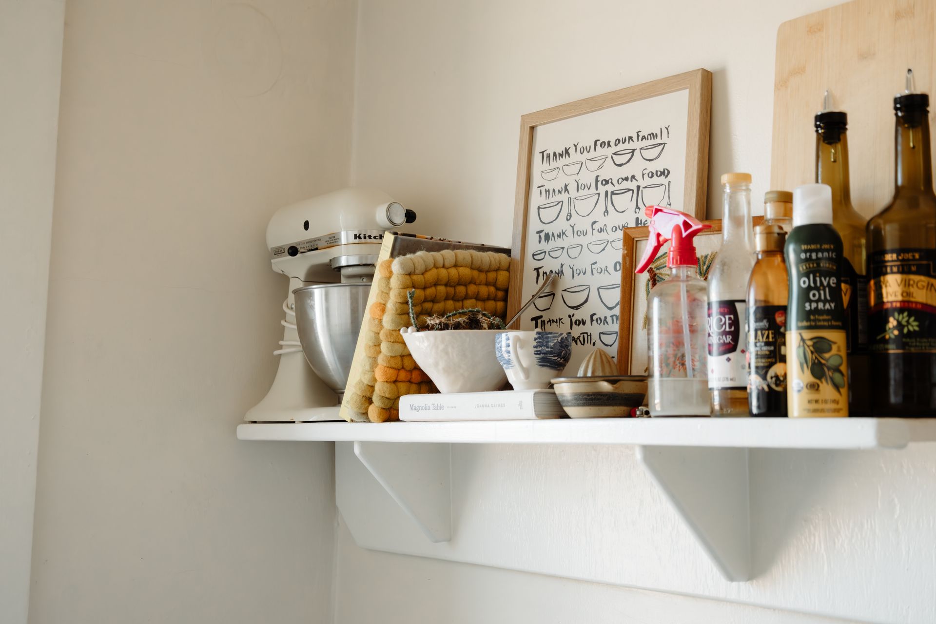 A white kitchen shelf filled with curated goodies, such as spices, cooking oils, a mixer, pot holders, and a piece of artwork. Apartments in Linden Hills by RightMove Properties.