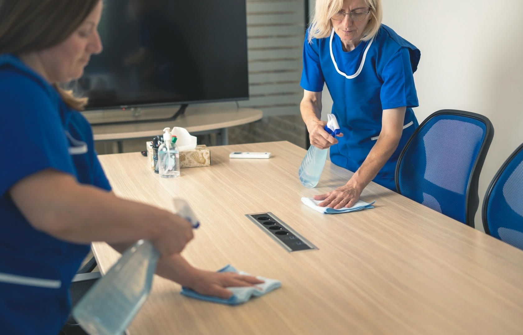 Two women are cleaning a conference table in an office.