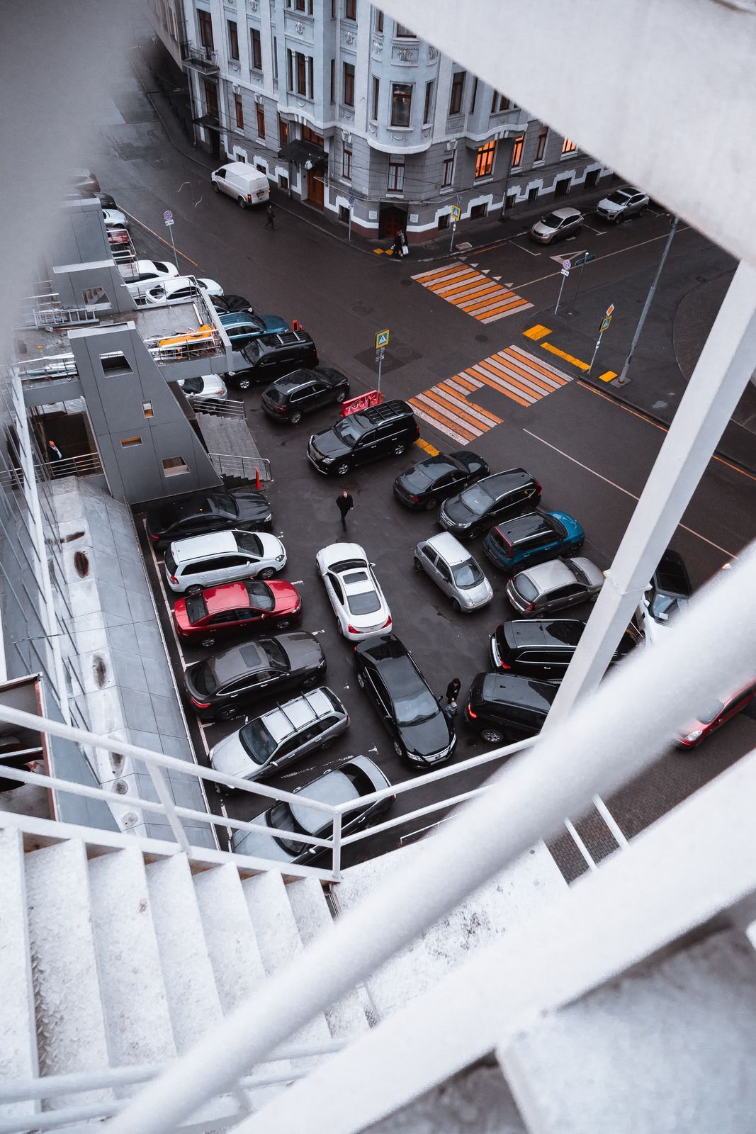 View of a parking lot with many cars from an elevated walkway, near a city street.