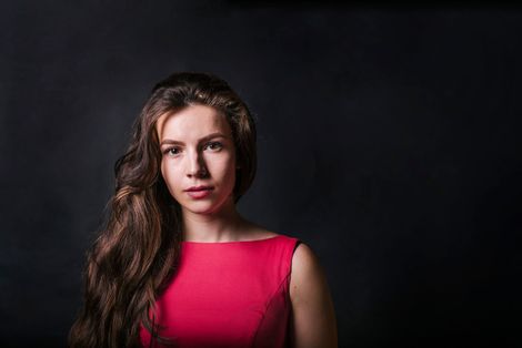 Woman with long wavy hair in a pink top against a dark background