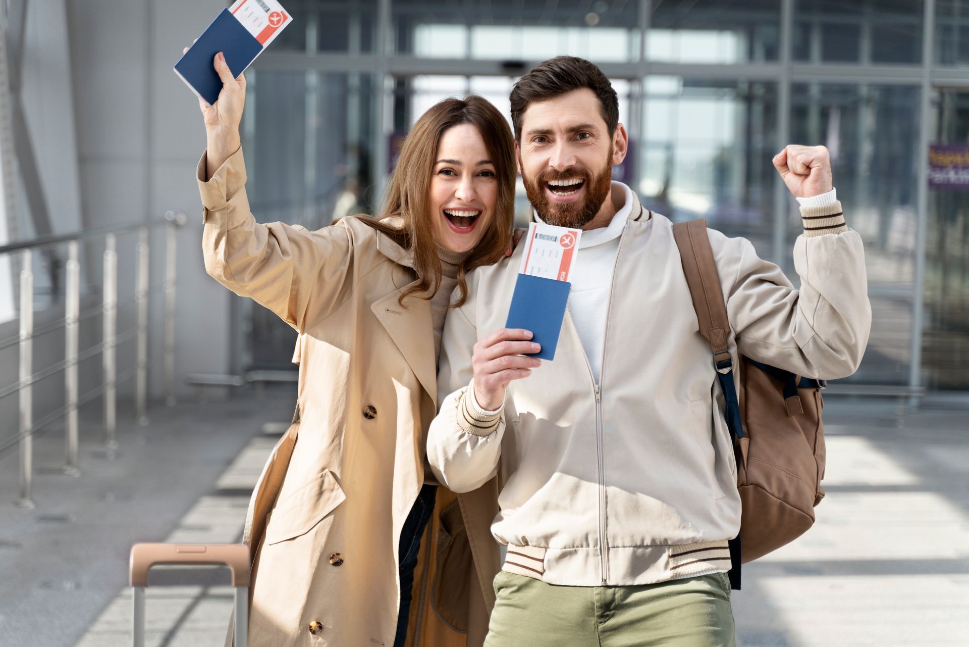 Two travelers in a terminal smiling and holding passports, celebrating with raised arms.