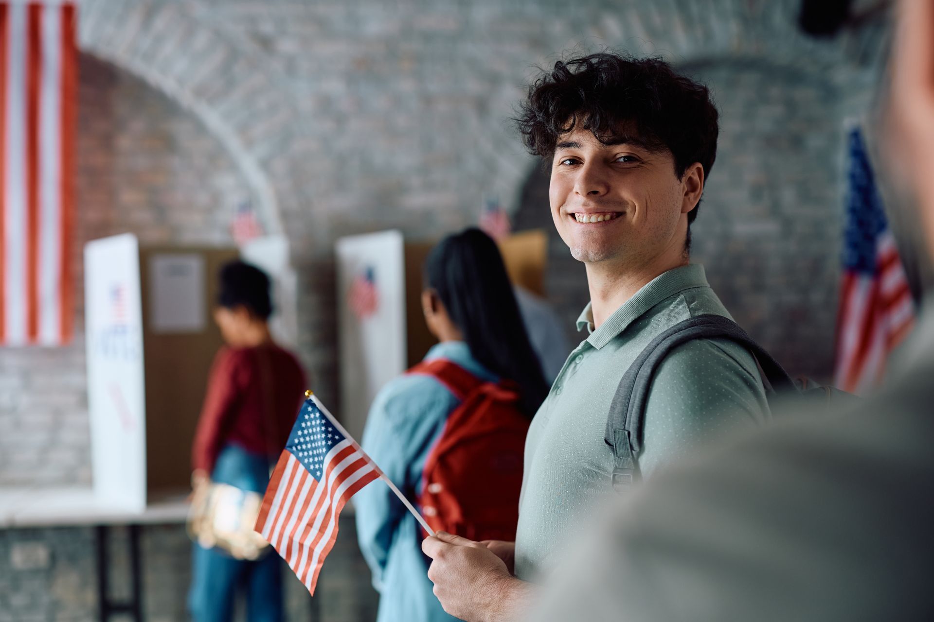 Student holding a small American flag in a school hallway, smiling at the camera