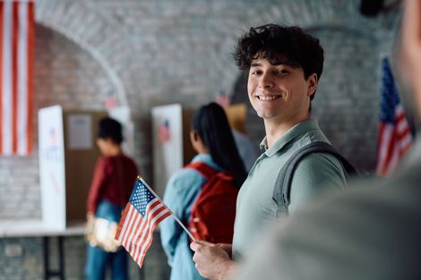 Student holding a small American flag in a school hallway, smiling at the camera