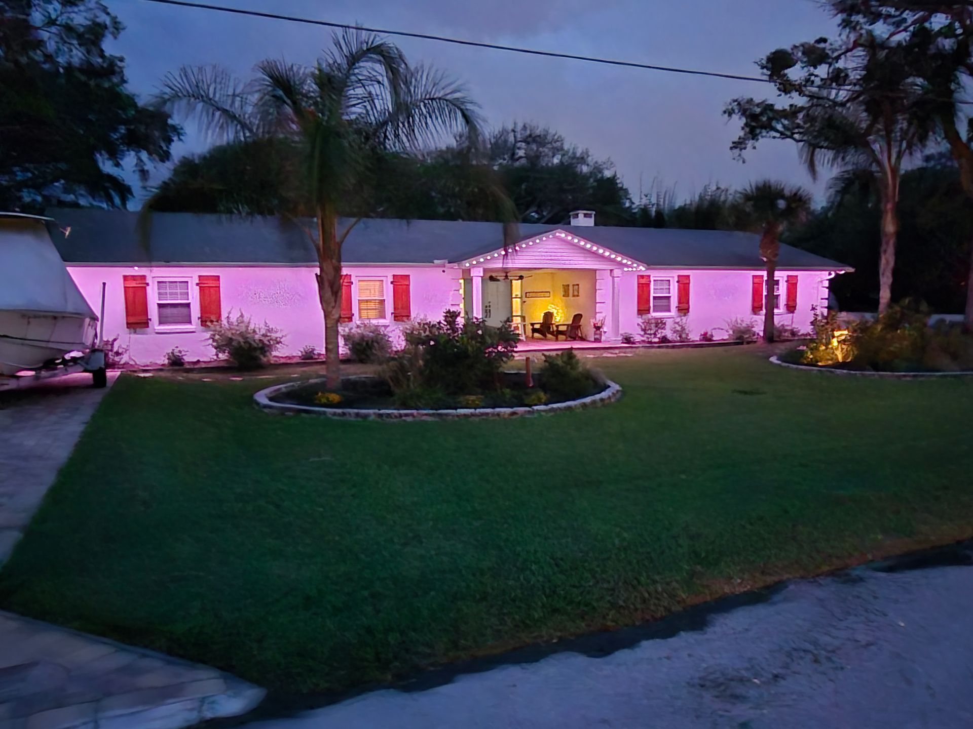 Single-story house lit pink at dusk, with a large lawn and palm trees in front.