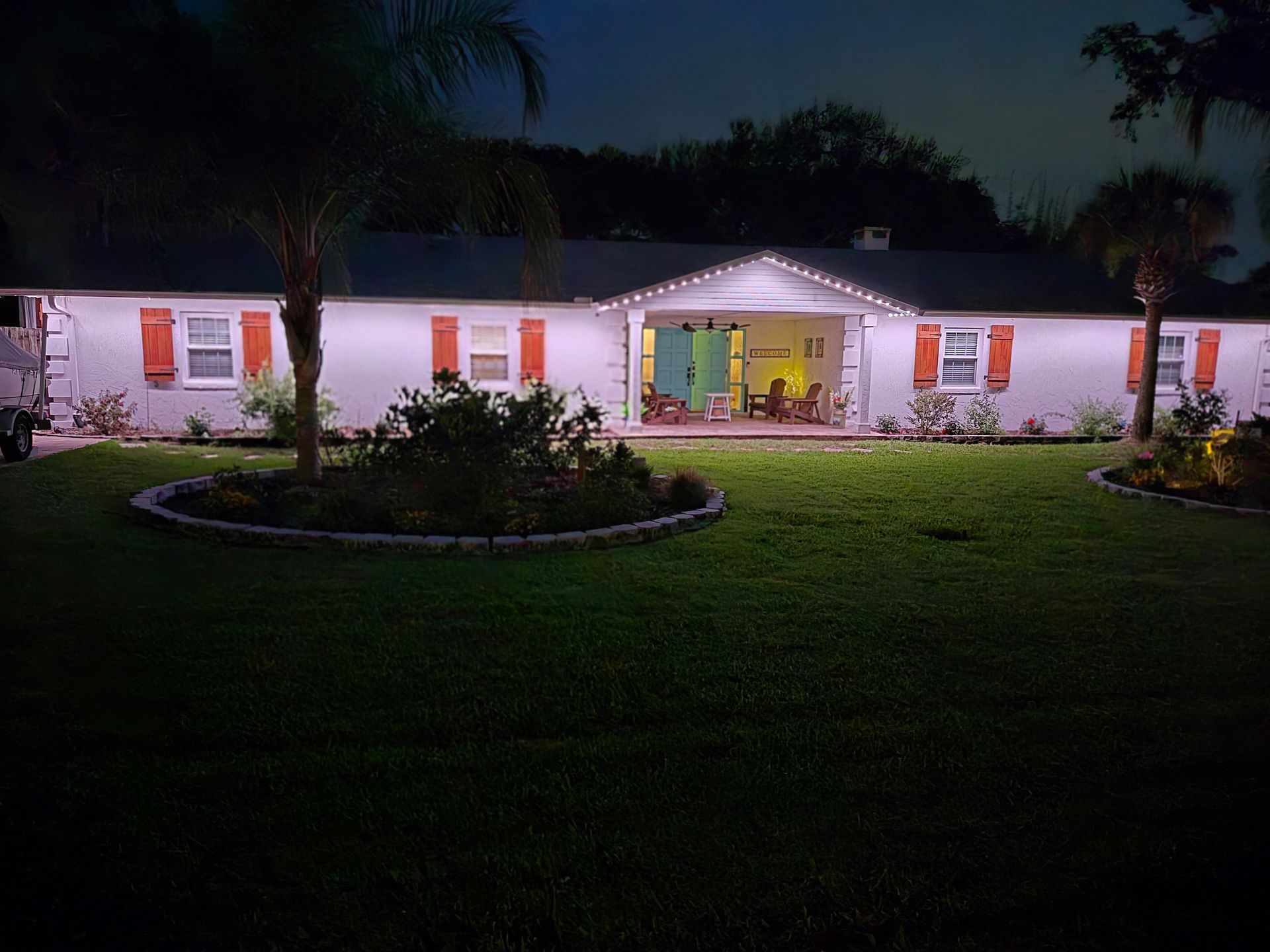 Single-story house at night with lit windows, a front porch, and a circular lawn garden.