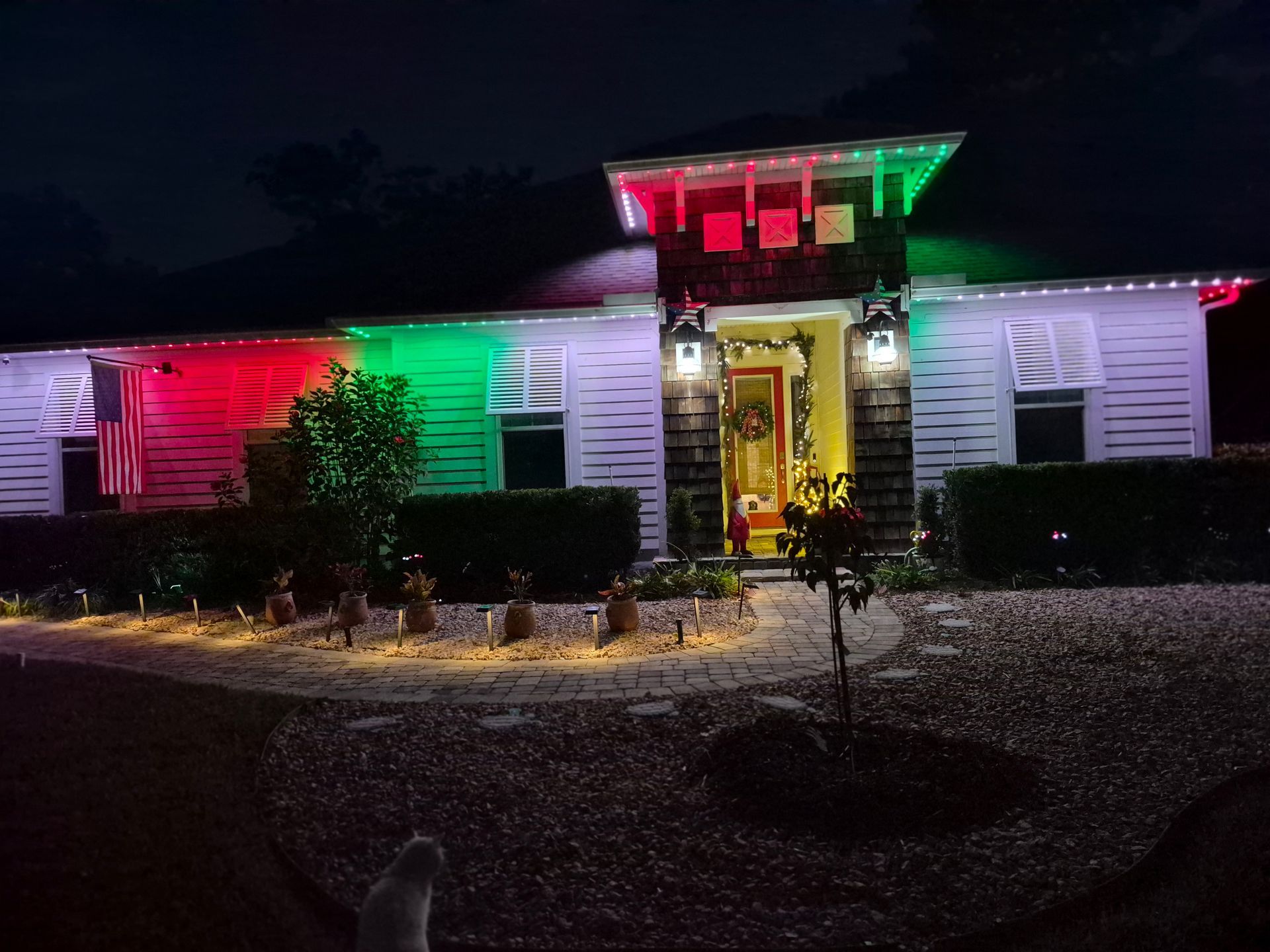House exterior lit with red and green holiday lights at night, glowing porch and windows