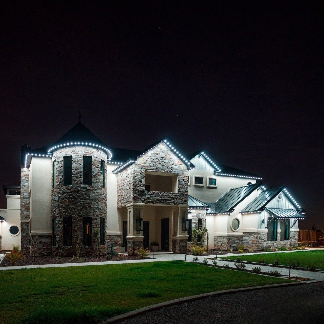 Large, well-lit modern house at night with white exterior, stone accents, and a green front lawn.