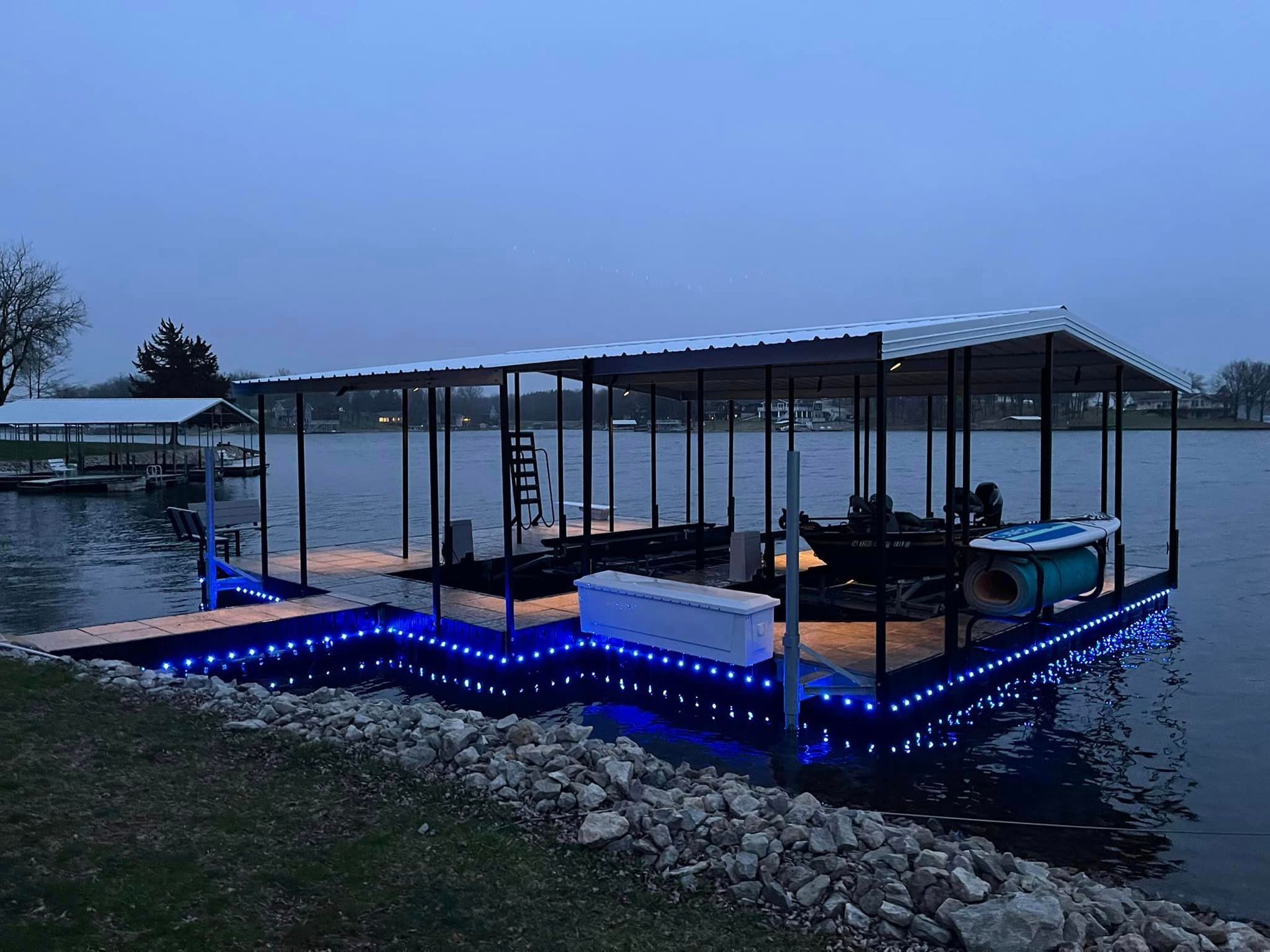 Floating dock at dusk with blue LED lights, metal railings, and covered seating on calm water