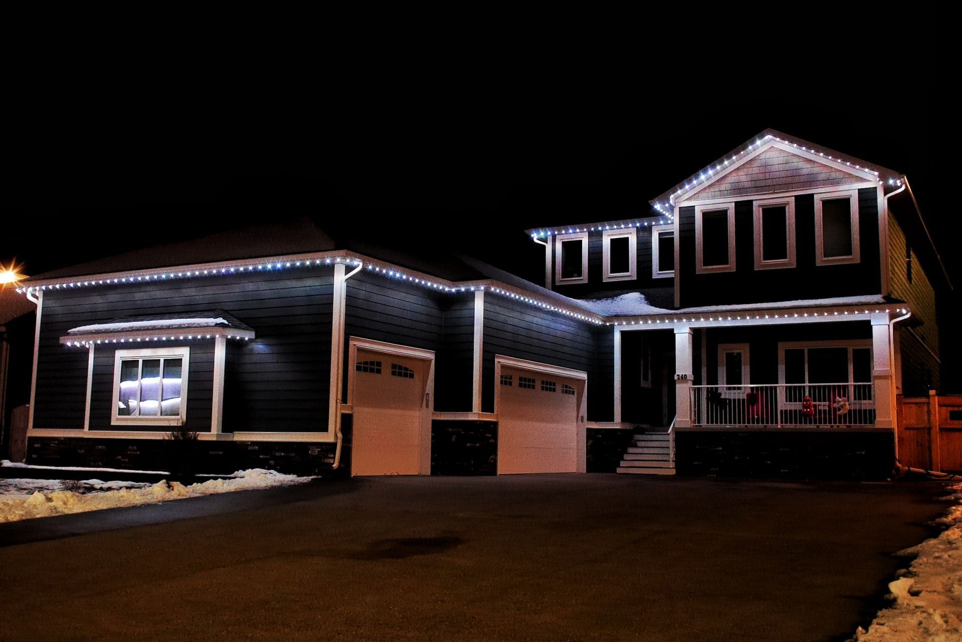 Nighttime view of a two-story house outlined with white holiday lights, with a garage and front porch.