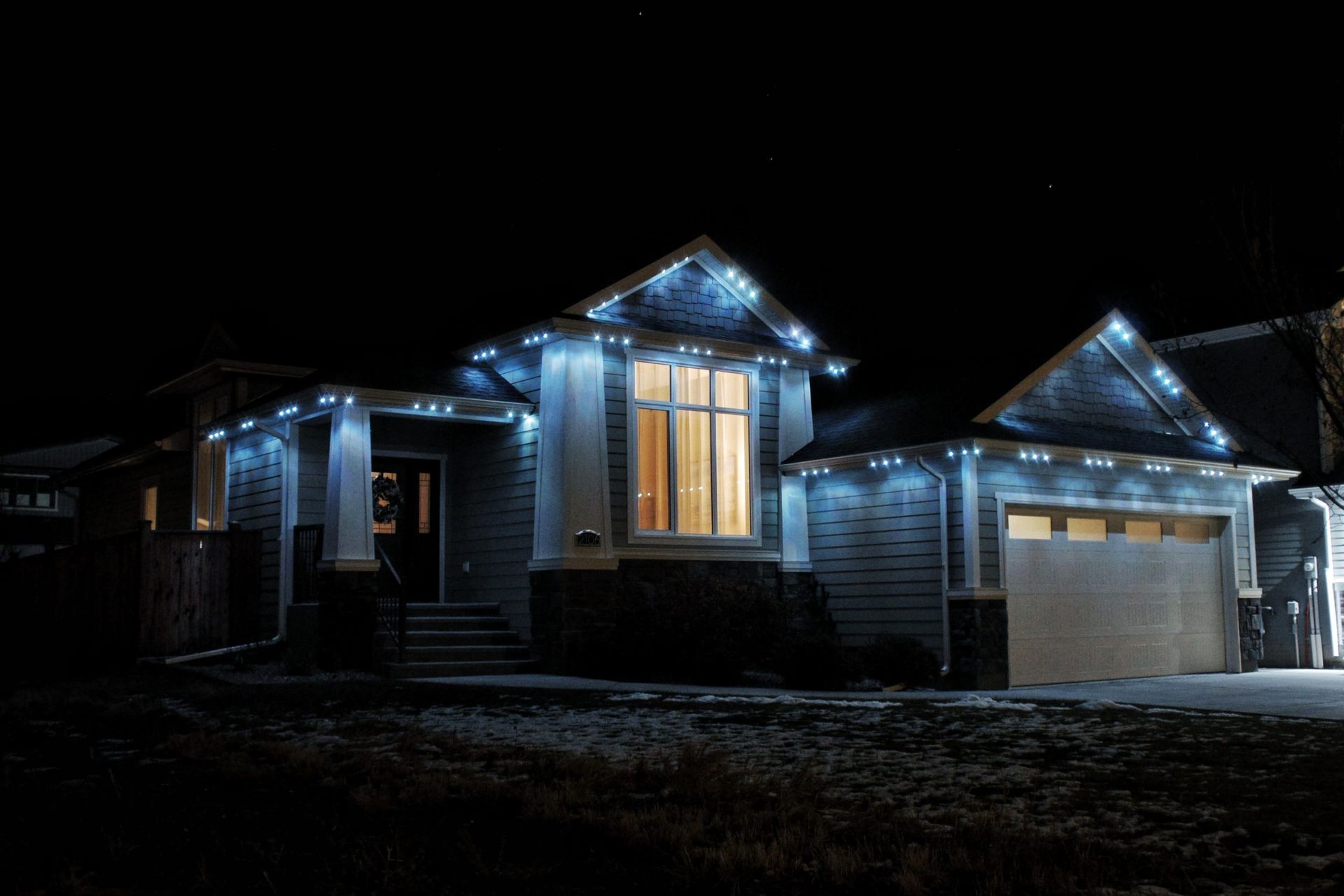 House exterior at night with blue holiday lights and a lit front window