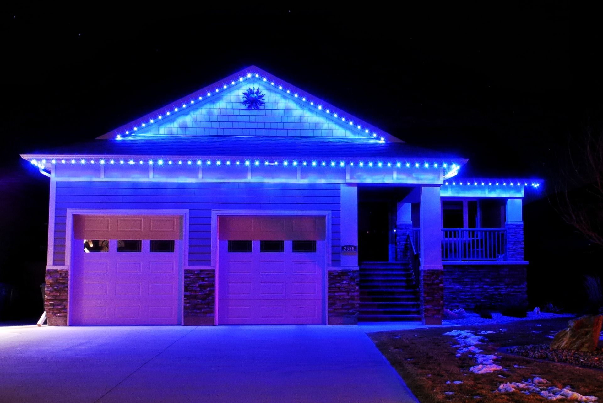 House with blue Christmas lights glowing along the roof at night