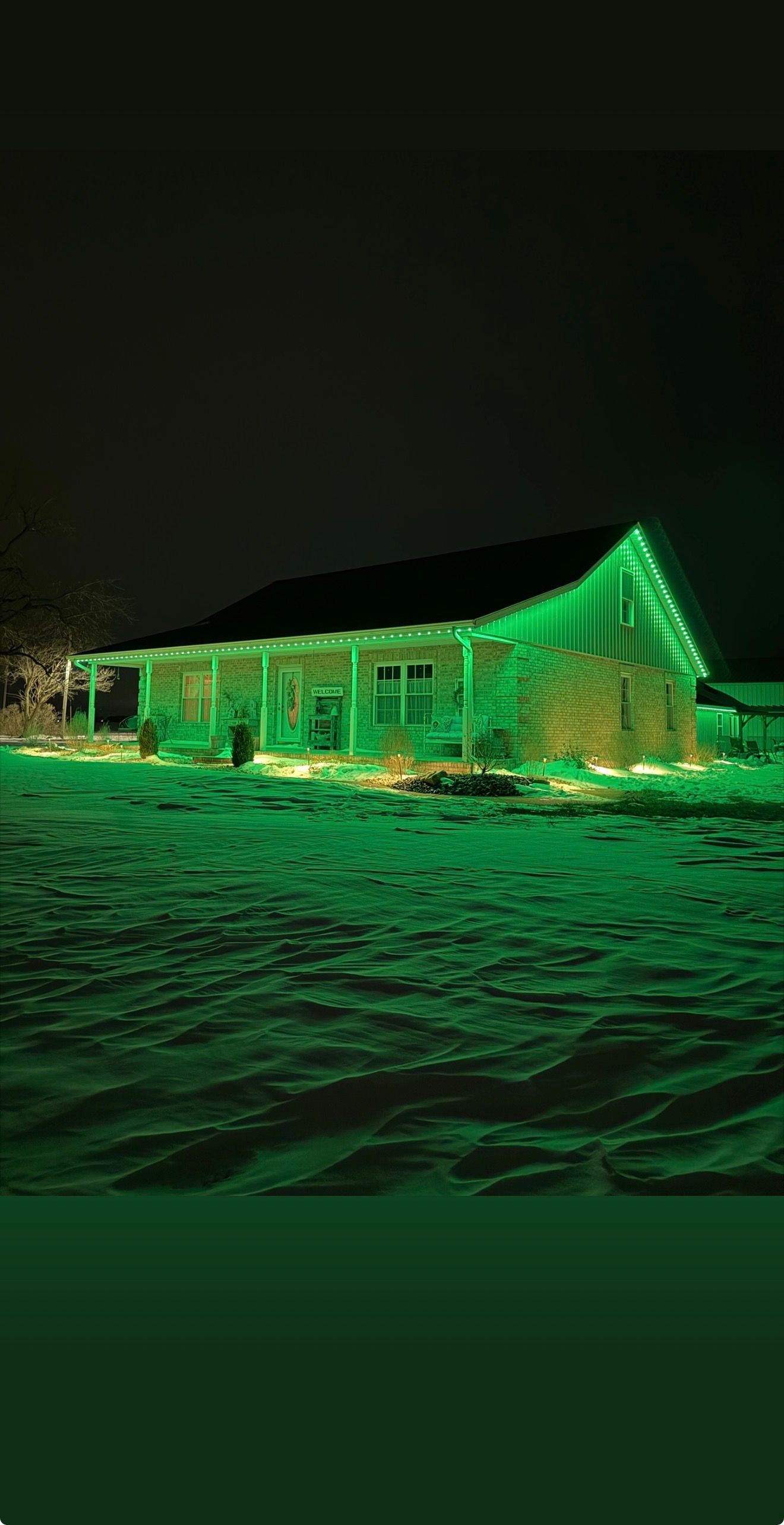 Green-lit house in a snowy field at night