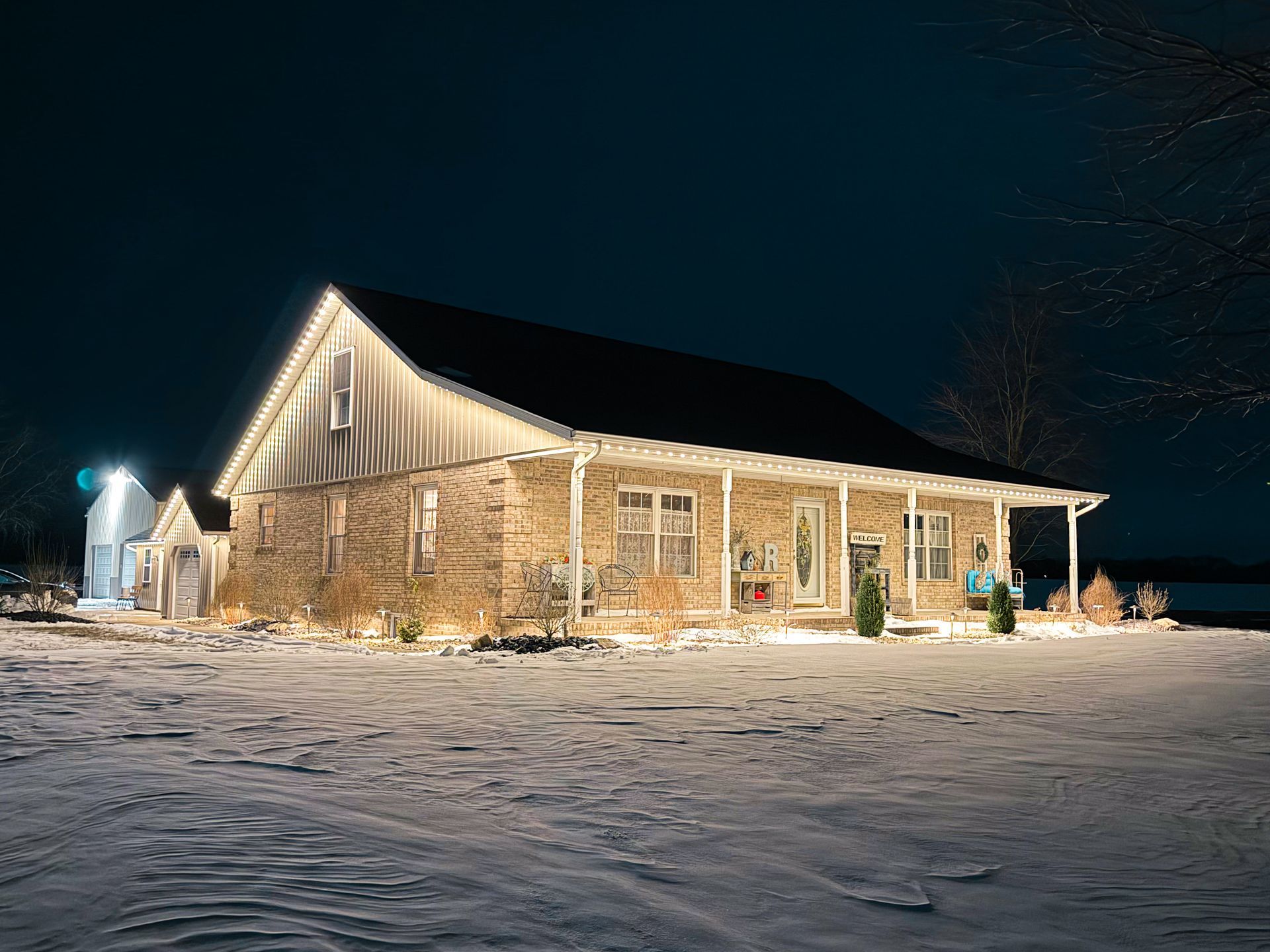 Snow-covered stone house lit warmly at night under a dark sky