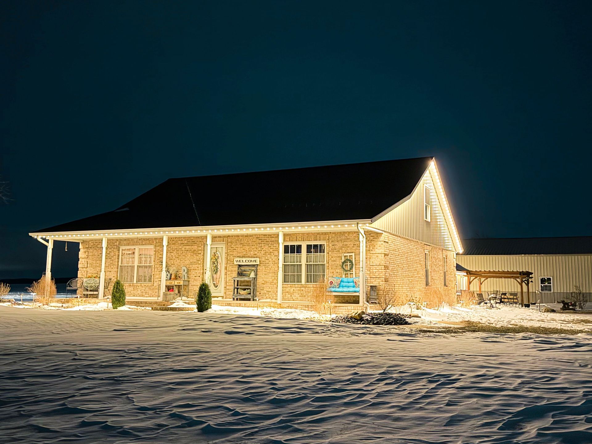 Snowy log cabin at night, lit with warm string lights against a dark sky.
