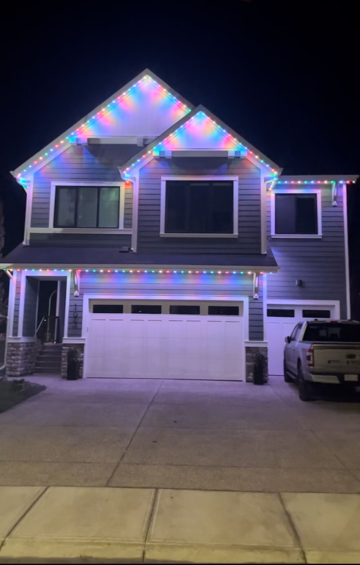 Two-story house at night decorated with colorful Christmas lights, garage and parked truck visible