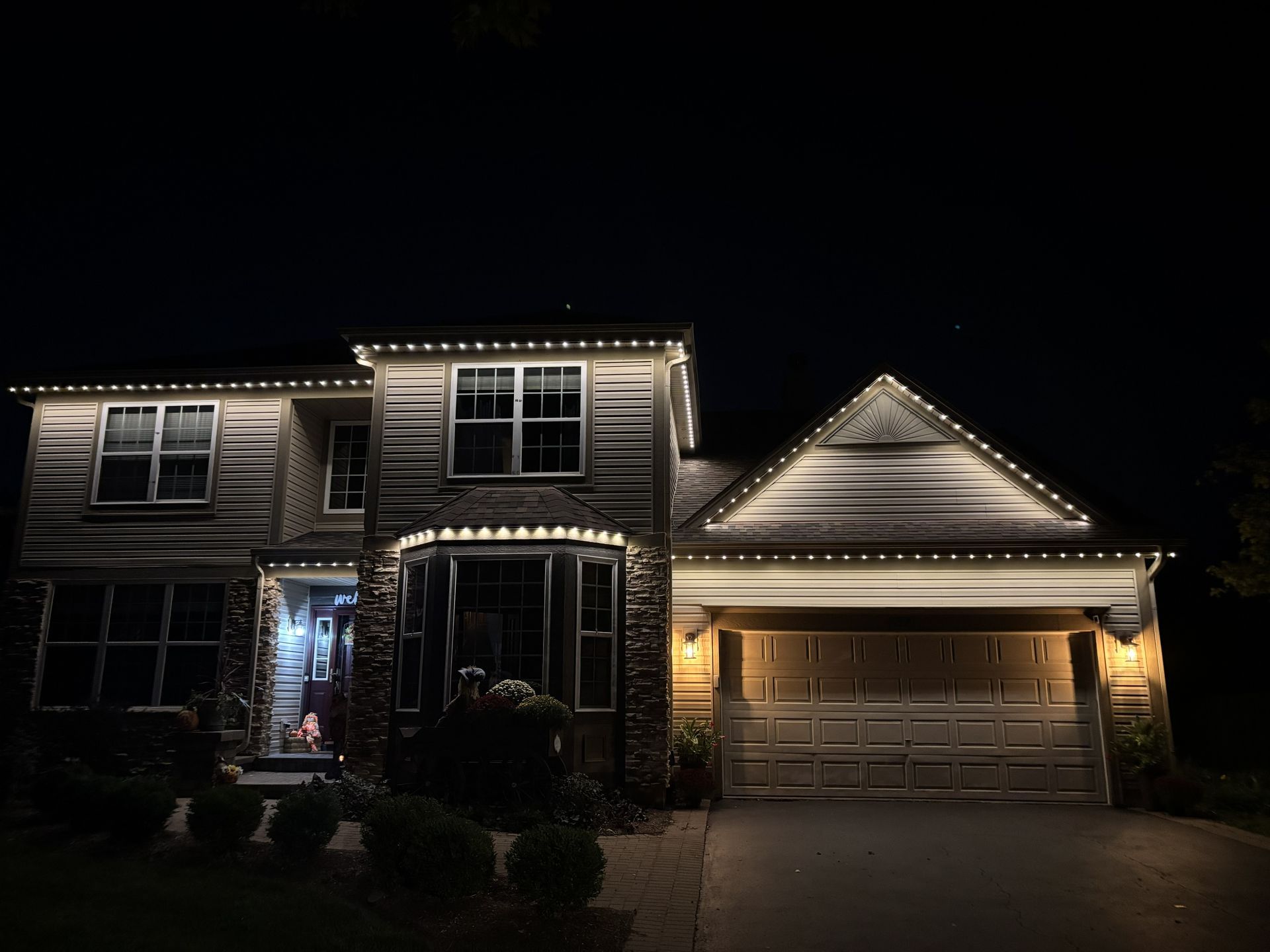 Two-story suburban house at night outlined with warm white holiday lights