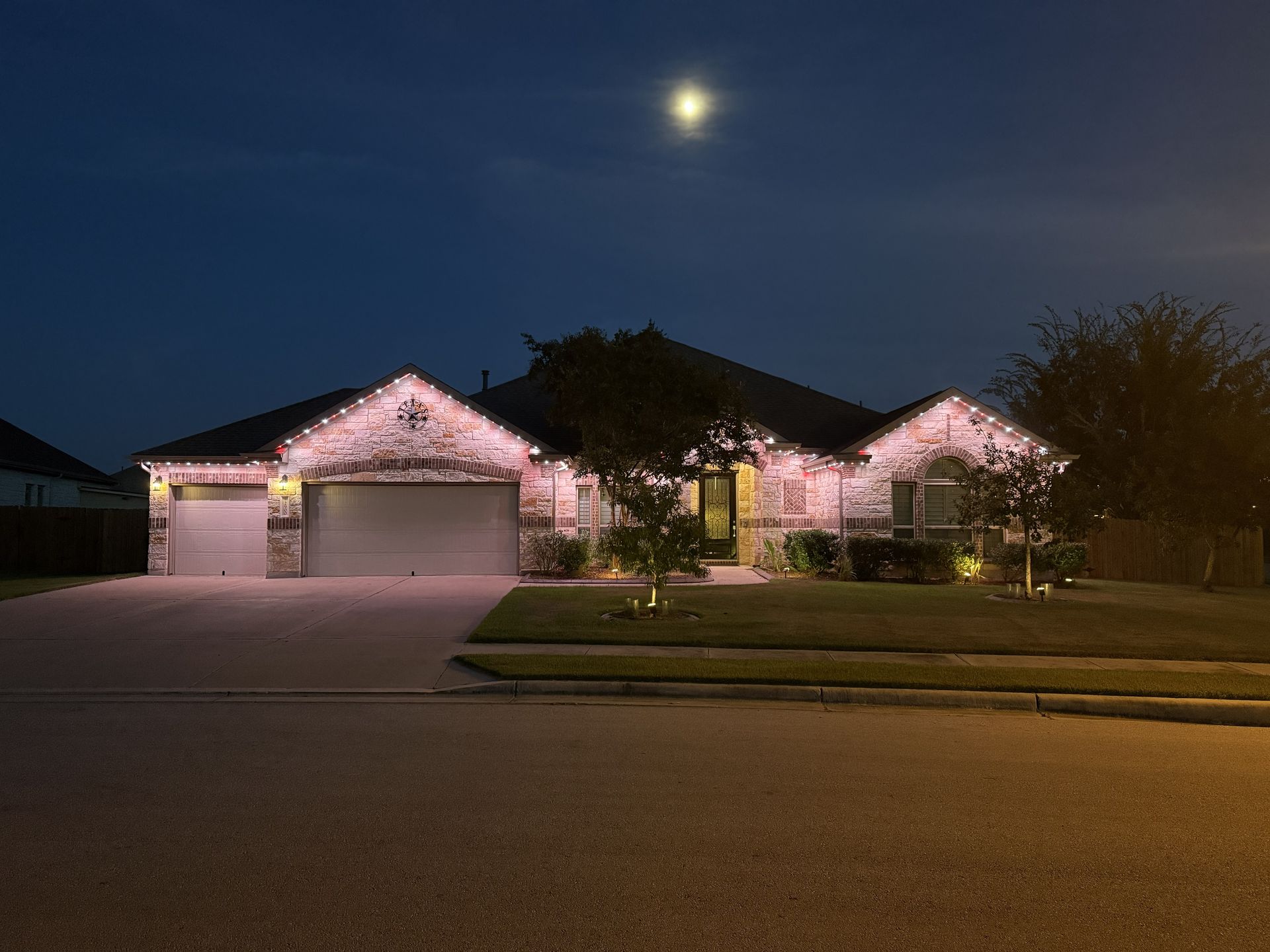 Suburban house lit pink at night with a bright moon overhead and a driveway in front