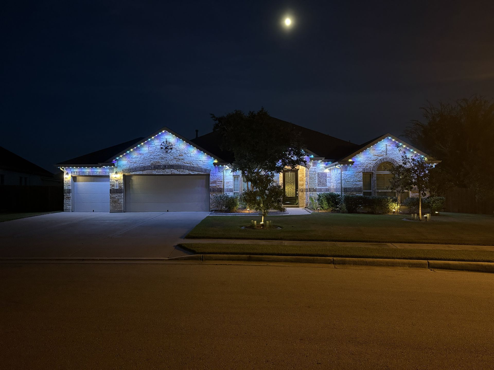 Suburban house at night with blue holiday lights and a full moon overhead
