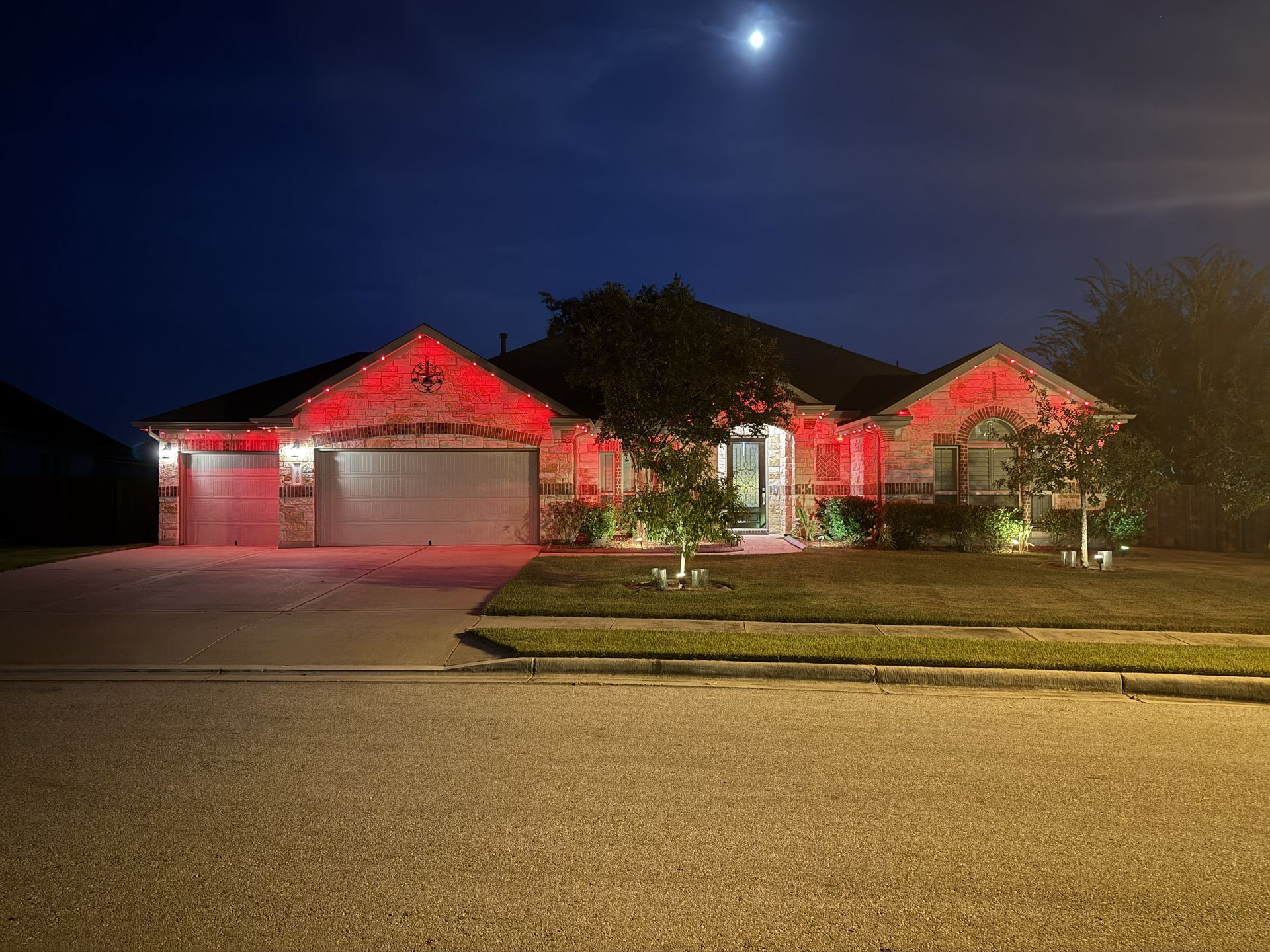 Single-story house at night with red holiday lights and a full moon overhead