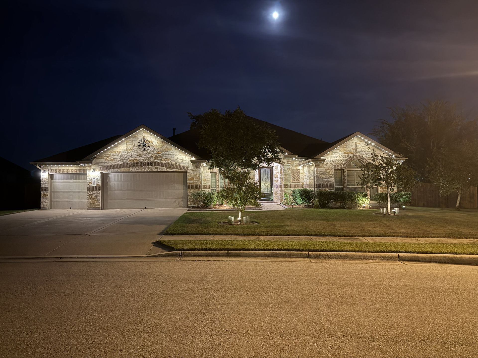 Suburban house lit at night with garage, front lawn, and moon overhead