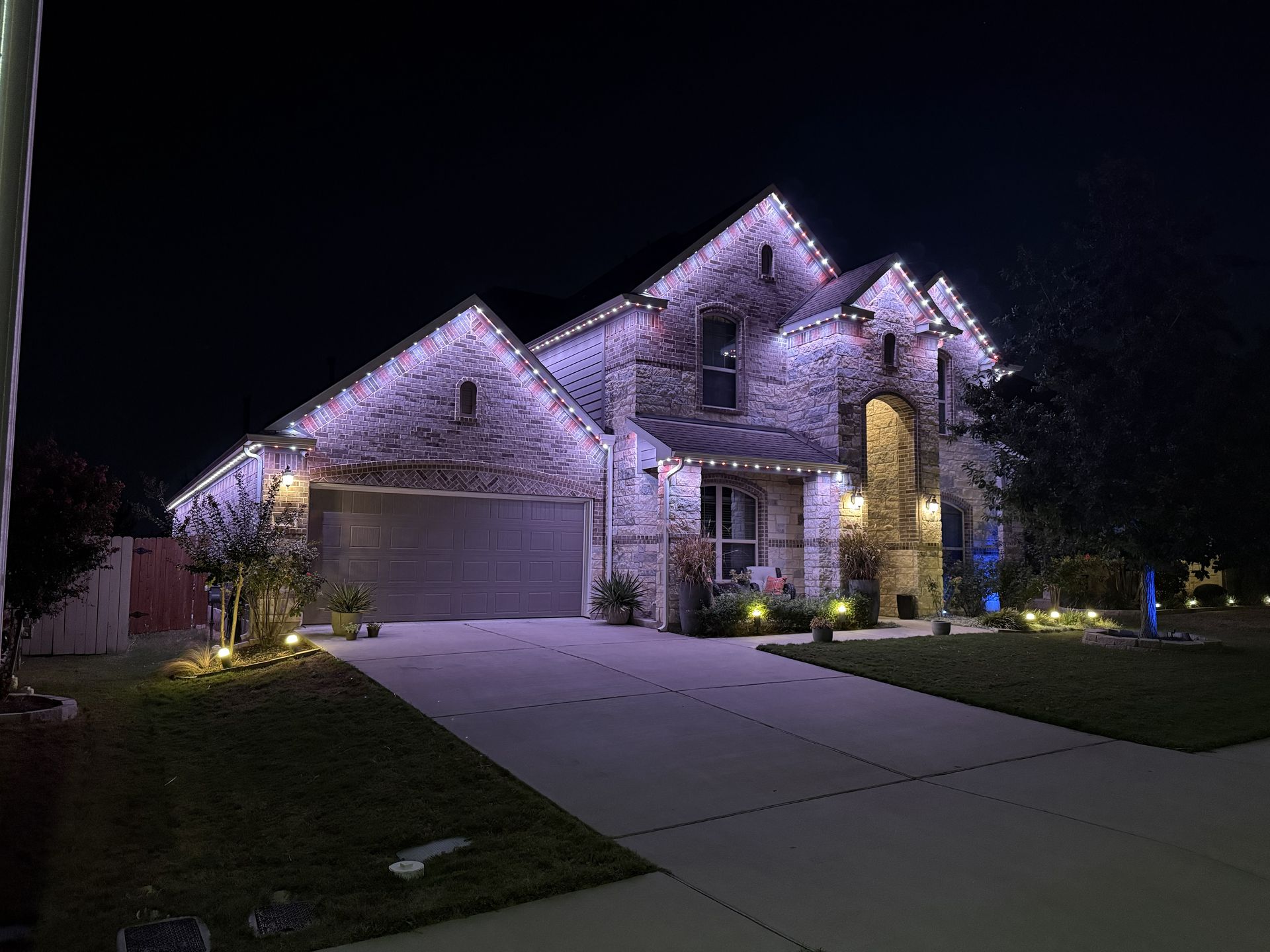 Brick house with lit purple roofline lights at night, driveway and lawn in front