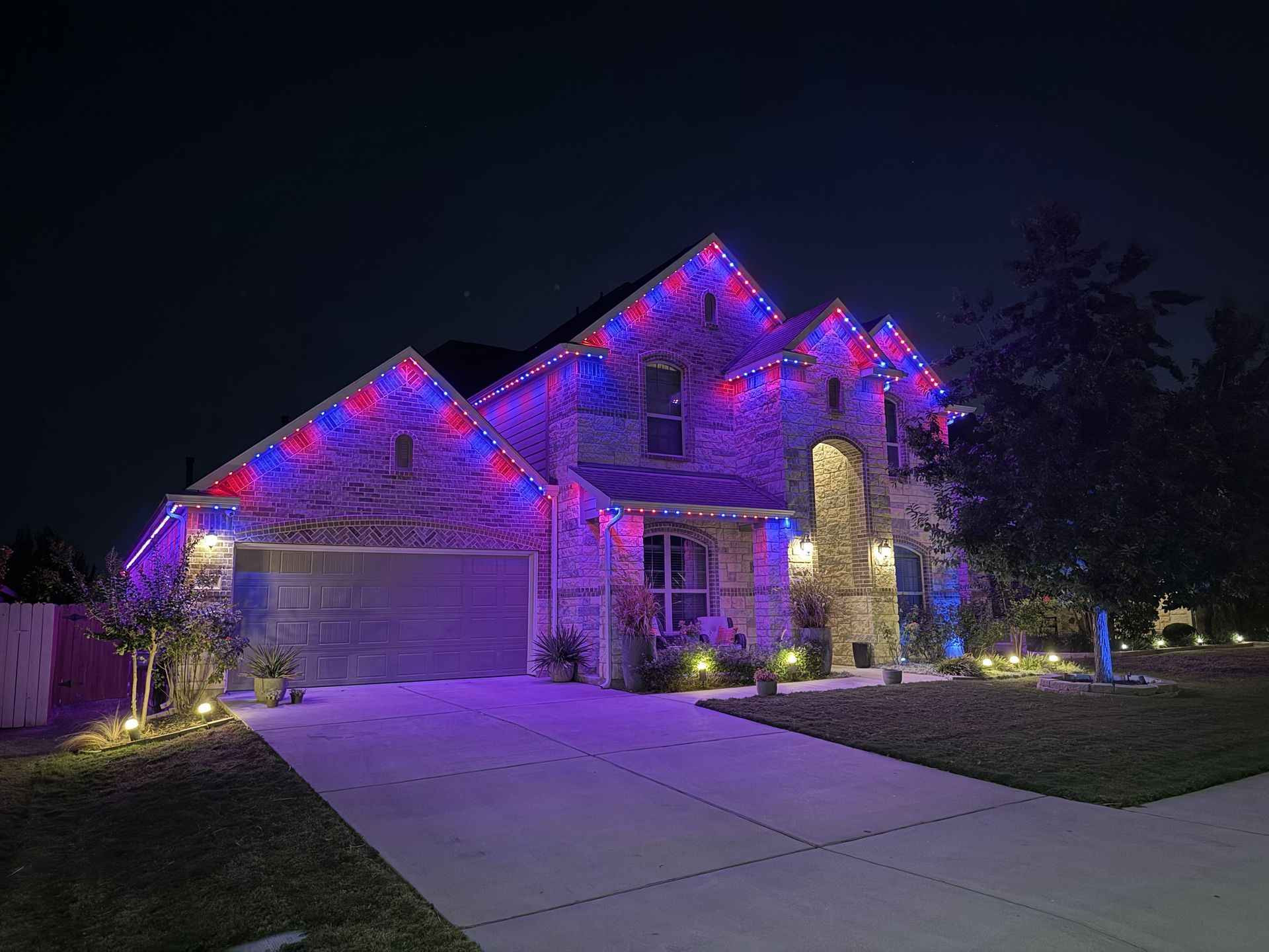 Two-story suburban house lit with purple and pink holiday lights at night
