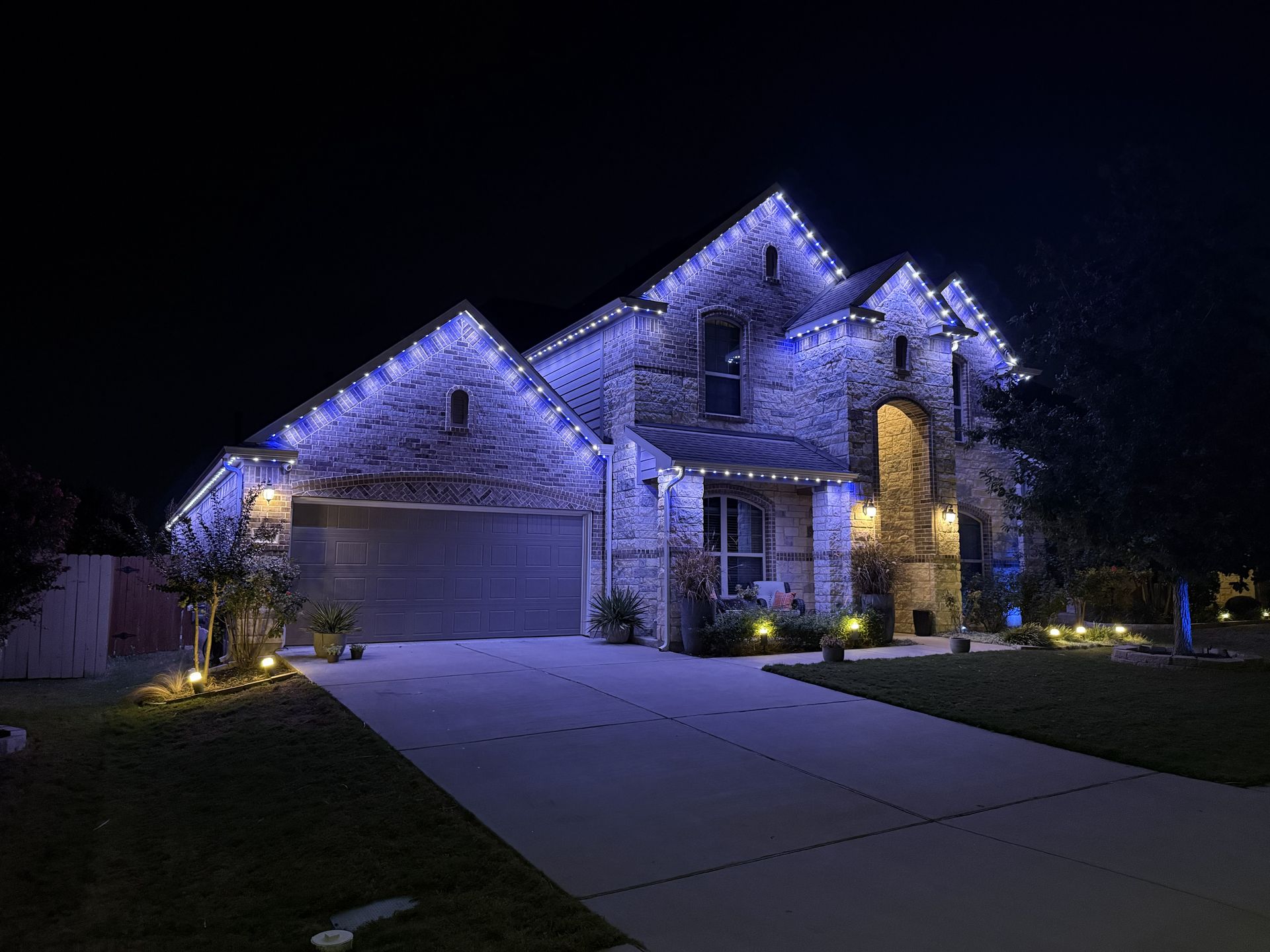 Stone house at night with blue accent lights and a lit driveway in front