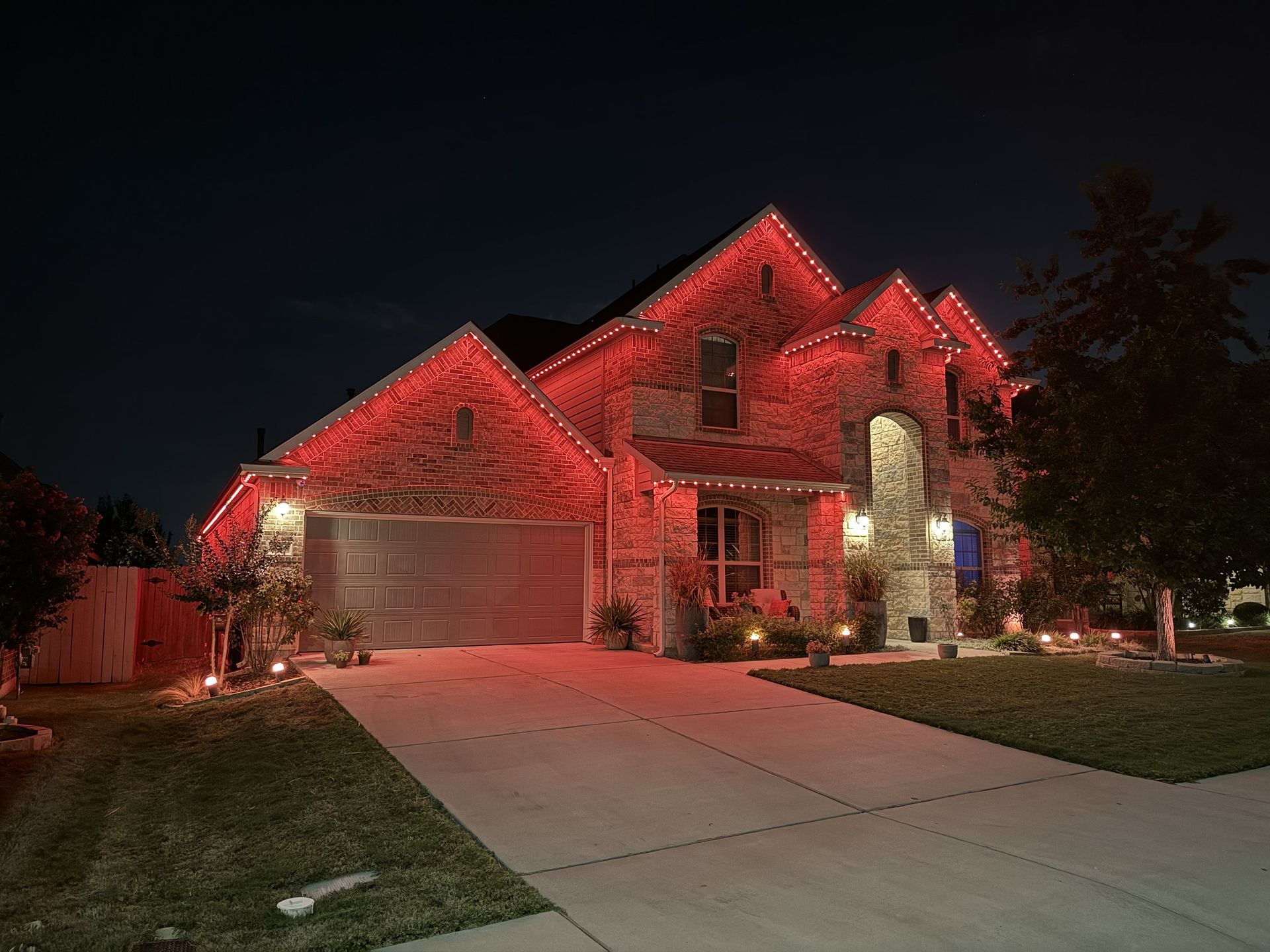 Suburban house at night, lit with red holiday lights and a glowing garage.