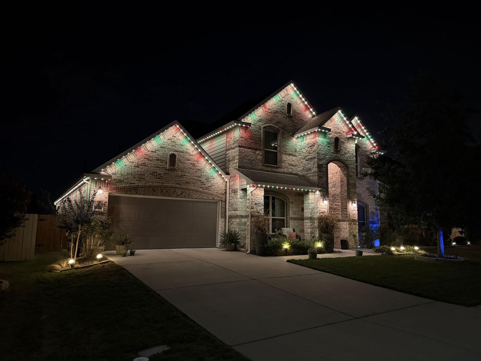Two-story suburban house at night with holiday lights along the roofline and driveway illuminated.