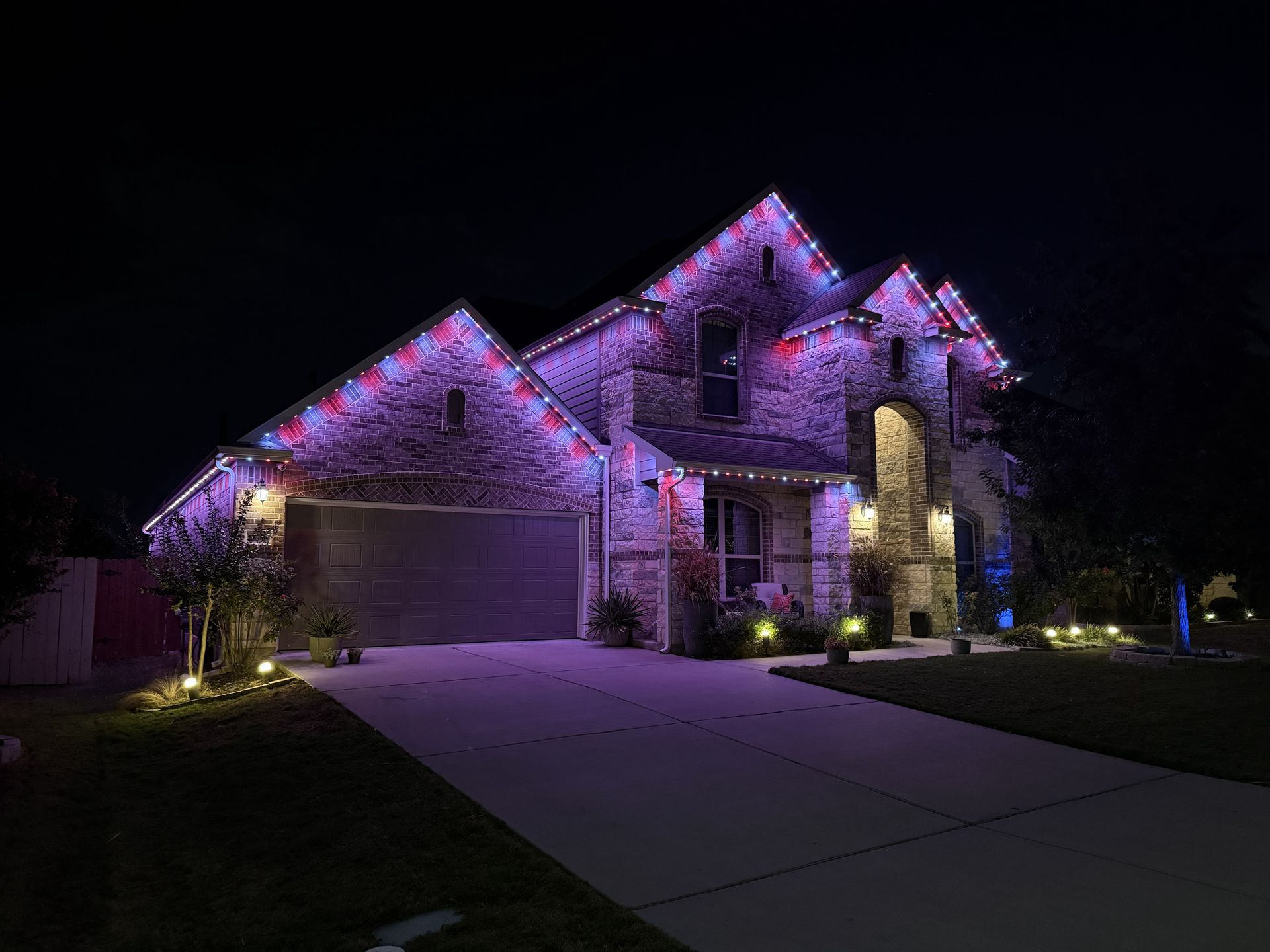 Suburban house at night with purple accent lighting, lit windows, and a driveway leading to the garage