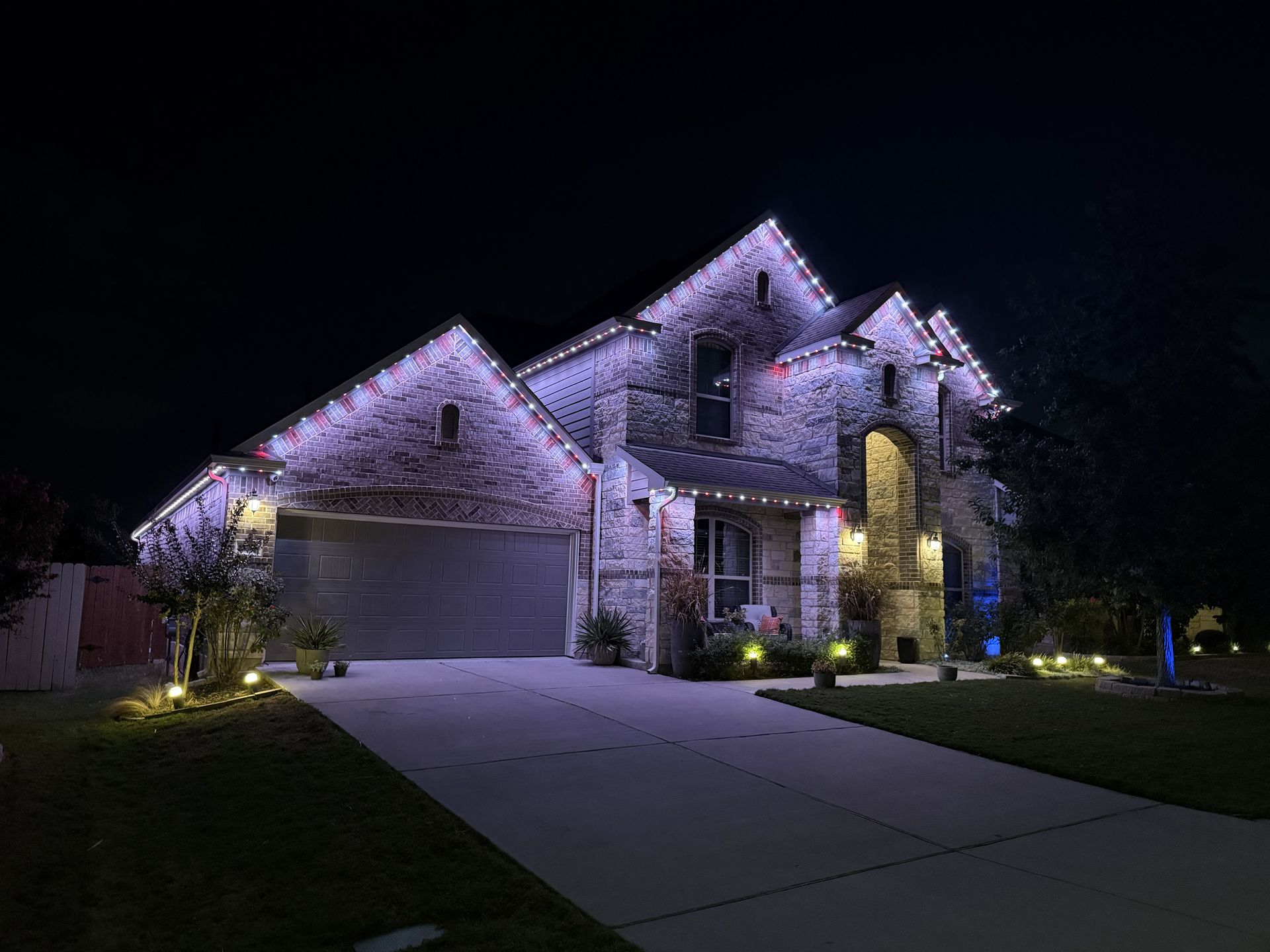 A lit suburban house at night with a stone facade, garage, and driveway