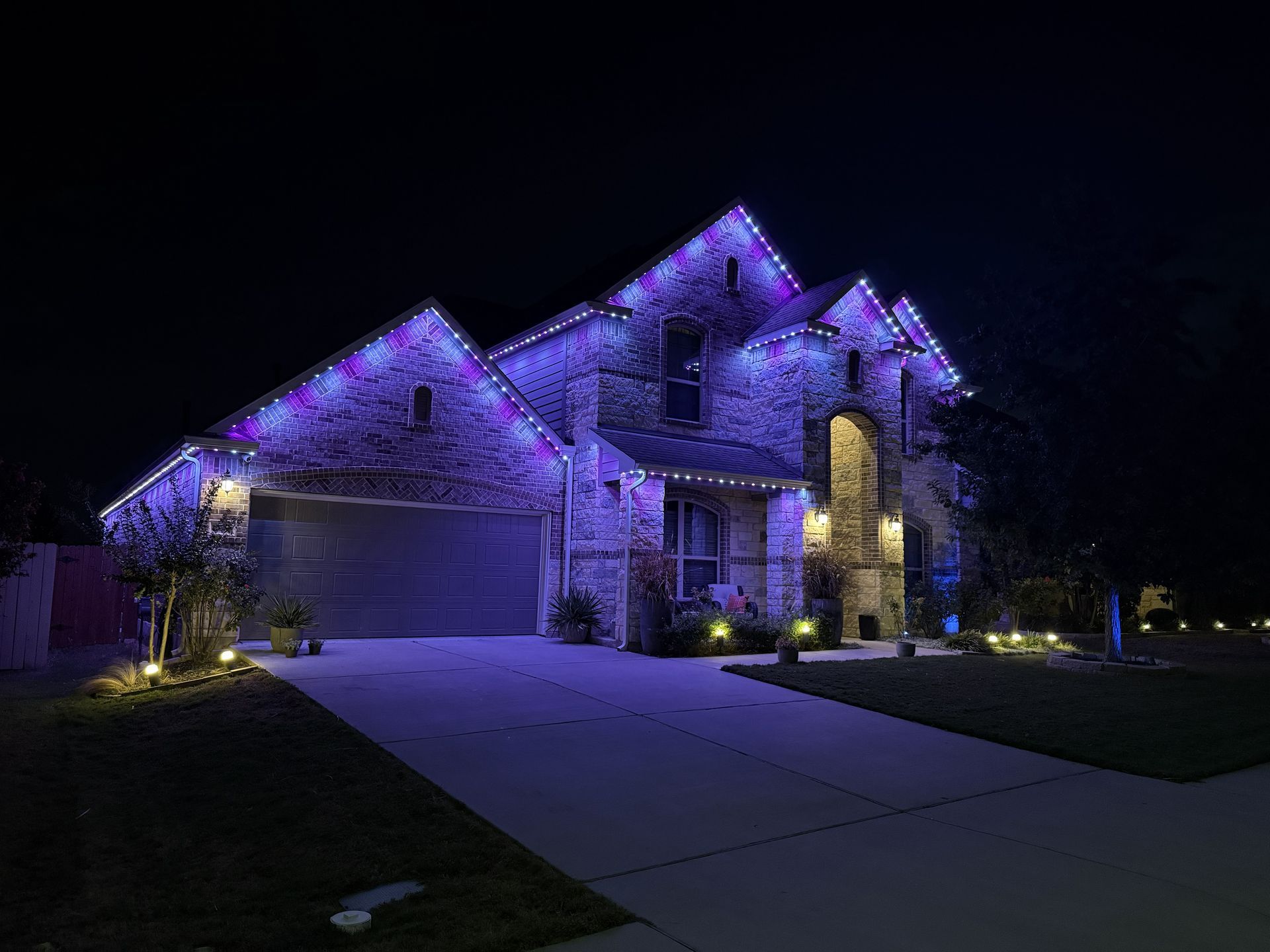 Two-story suburban house lit with purple lights at night, with a driveway and garage visible.