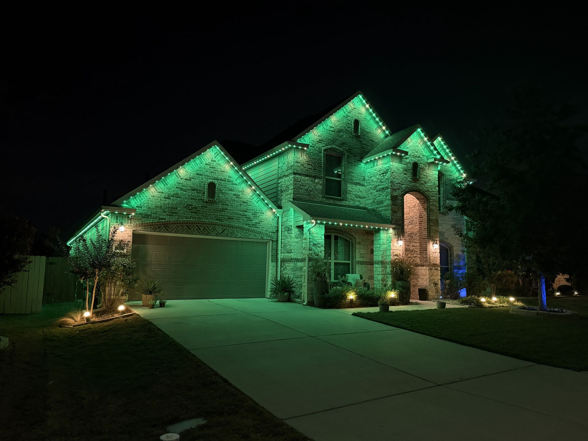 House at night with green holiday lights illuminating the roof and garage