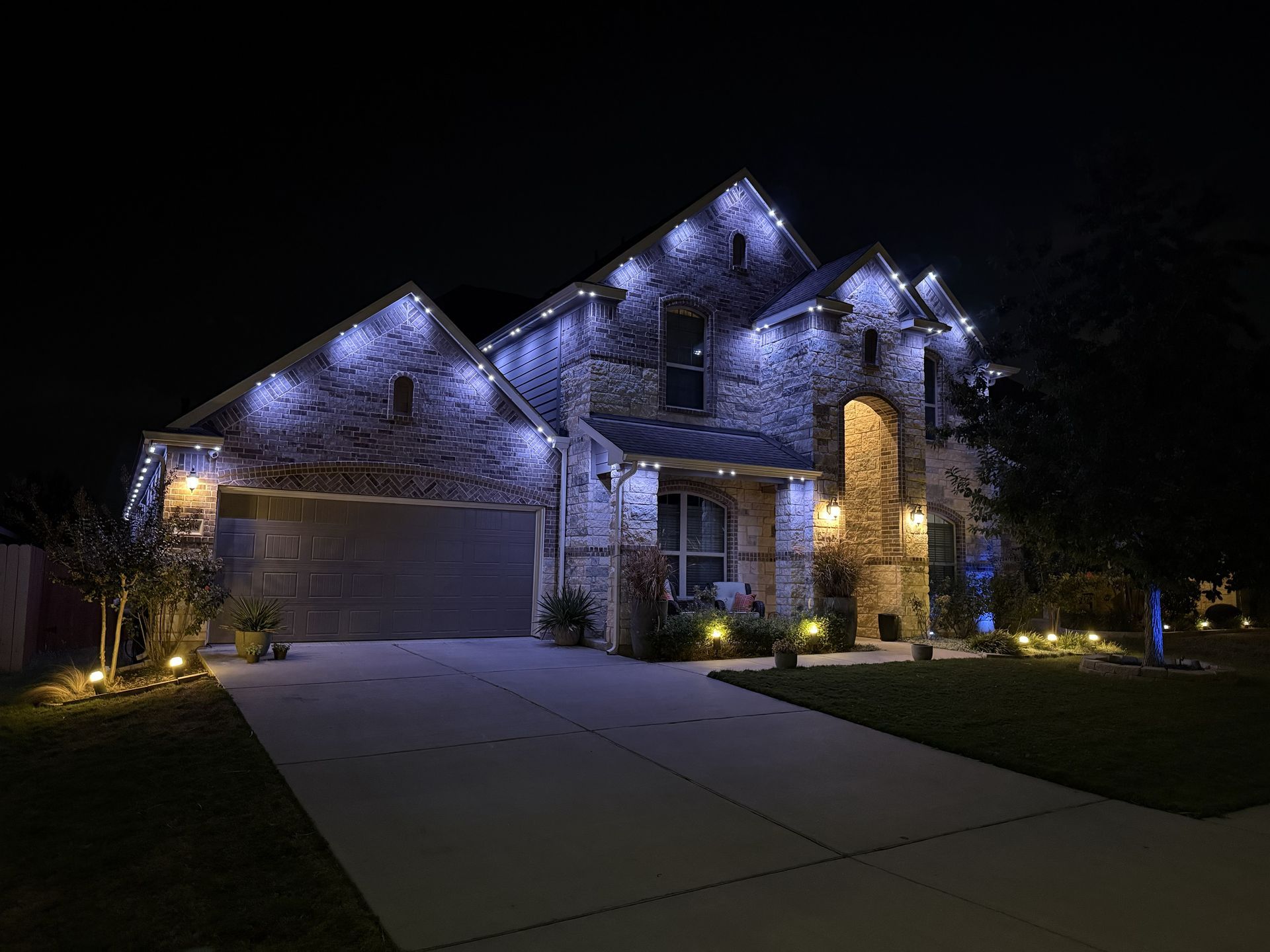 Well-lit suburban house at night with blue roof lights and a driveway leading to the garage