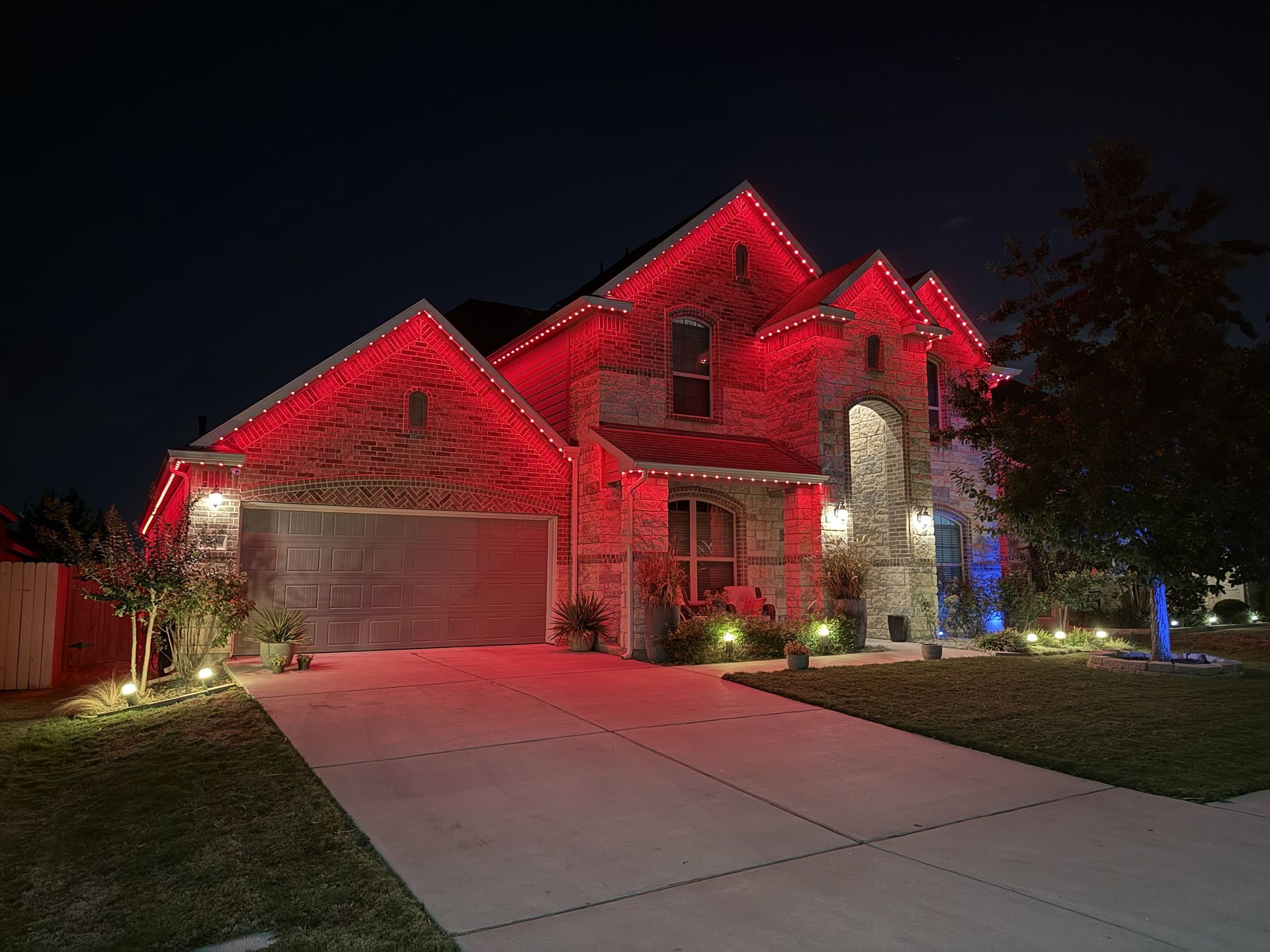 Suburban house at night lit with bright red exterior lights and a driveway in front