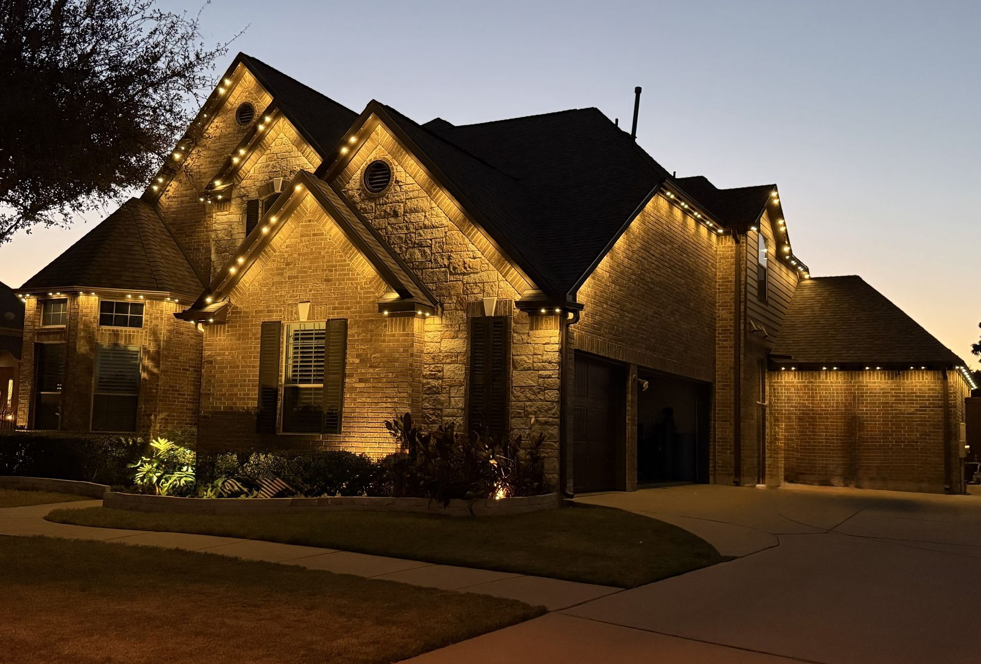 Brick house at night with warm exterior lights illuminating the facade and driveway