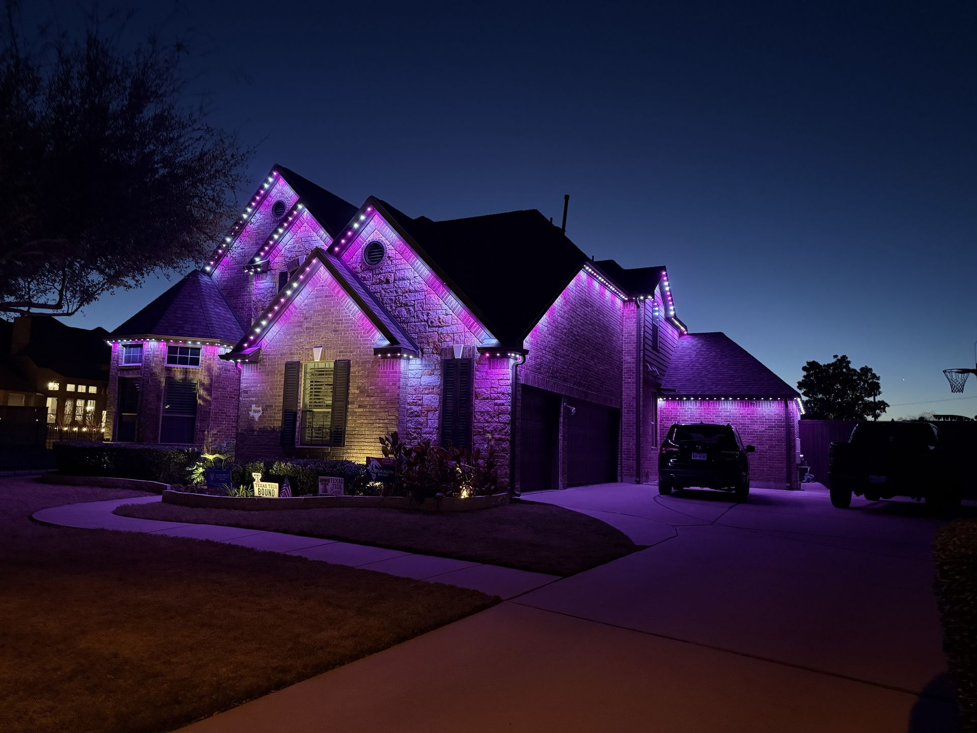 House lit with purple lights at dusk, with a driveway and garage on the right.
