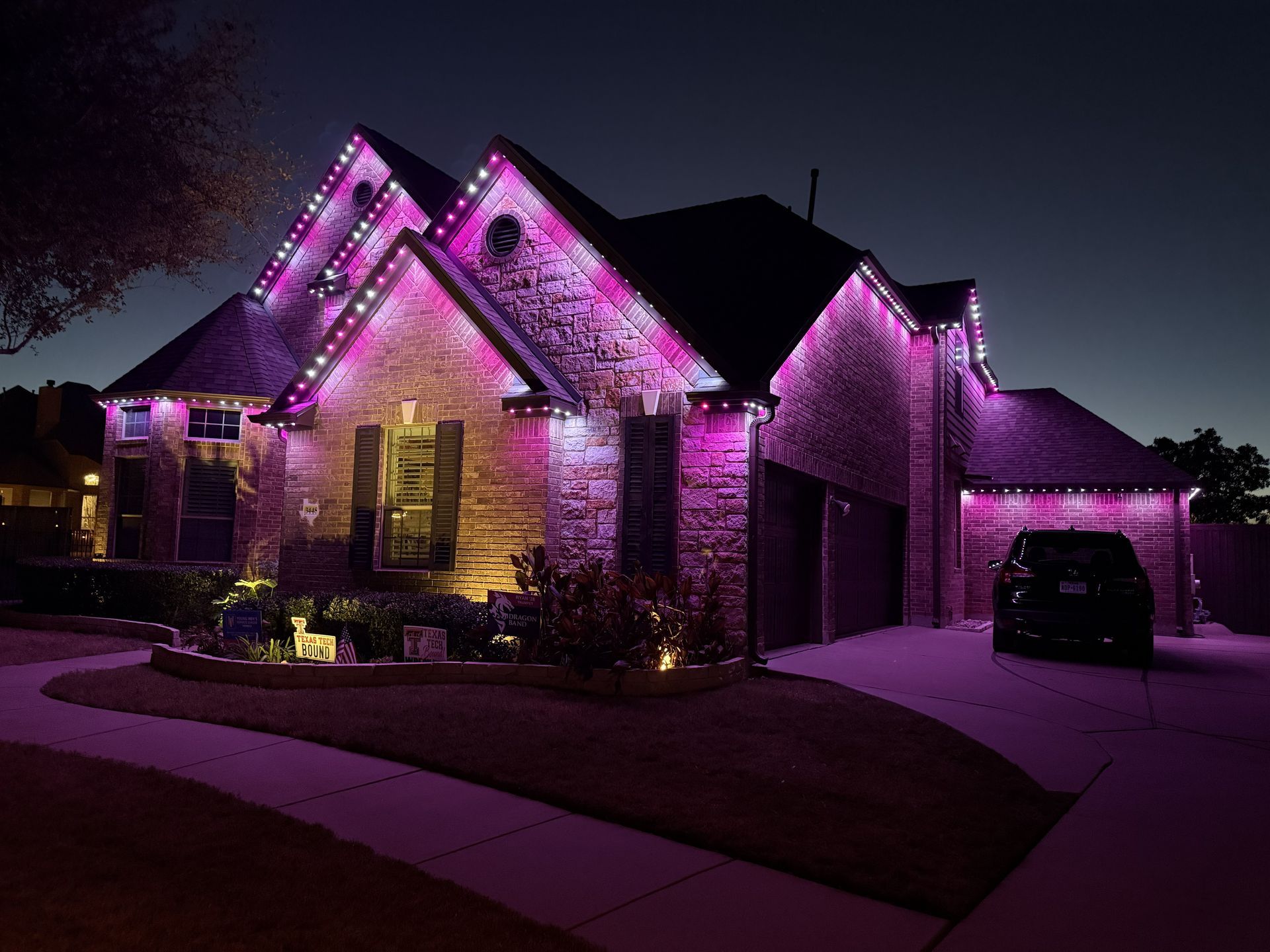 House lit with purple holiday lights at night, viewed from the street.