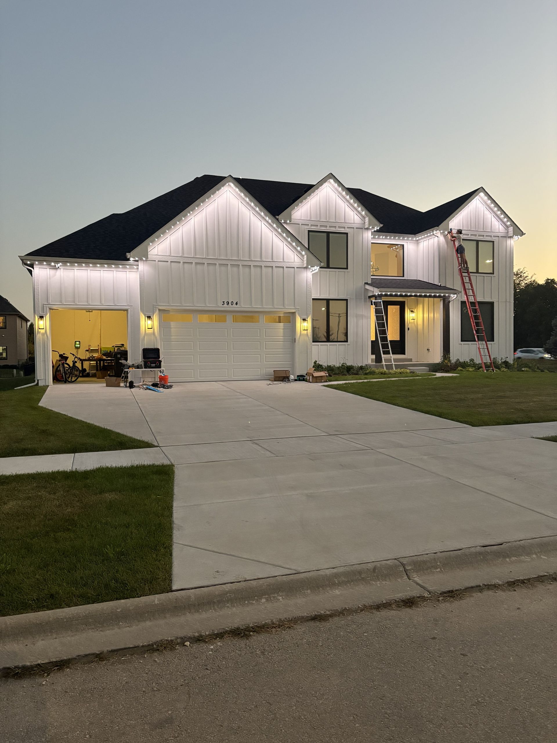 Two-story suburban house at dusk with white holiday lights and a wide driveway