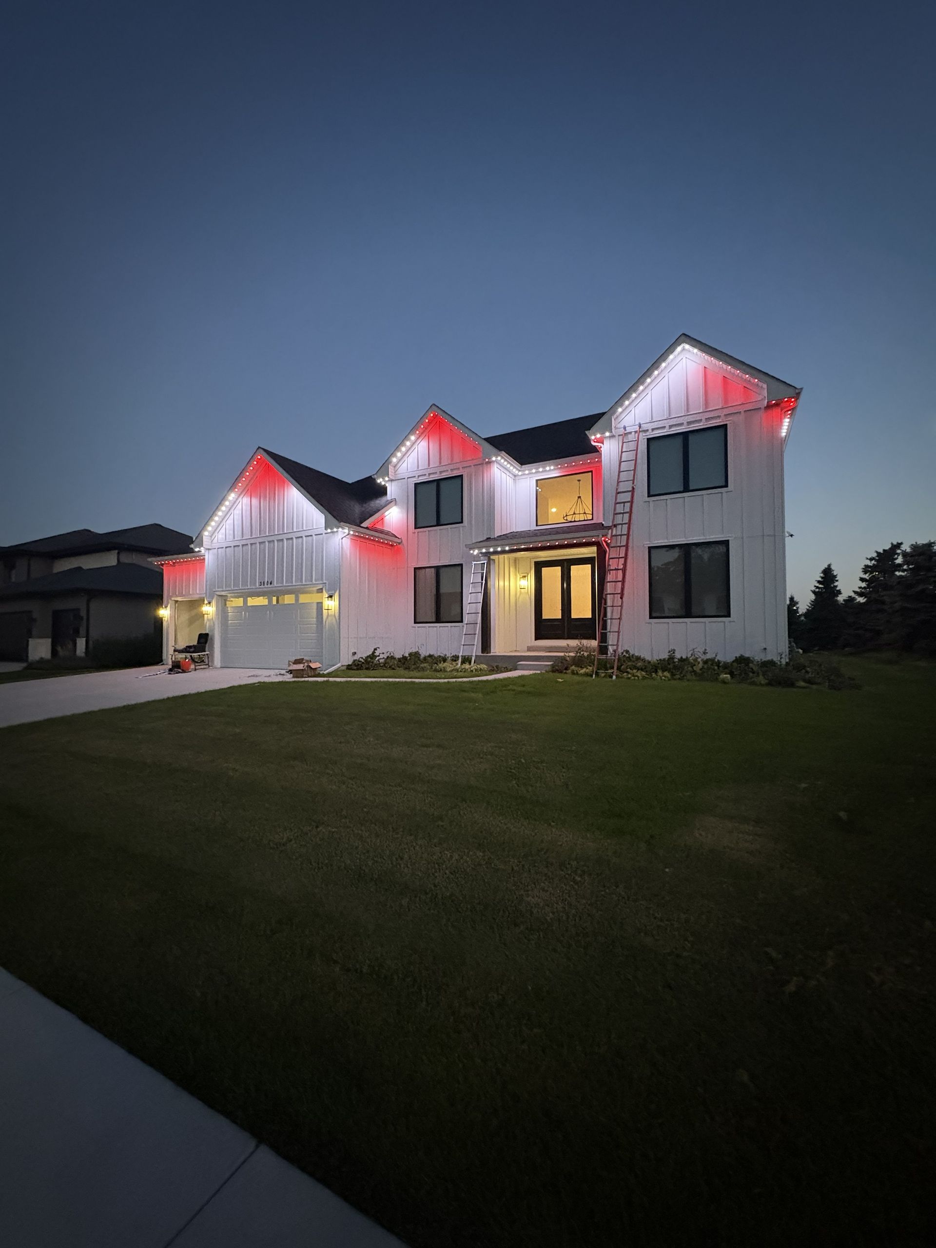 White two-story house with red roof lights at dusk, viewed from a grassy lawn.