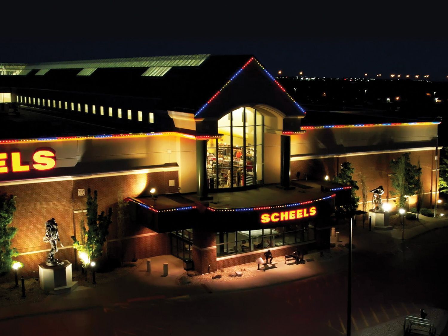 Night view of a Scheels store with bright red and yellow lights and a lit entrance