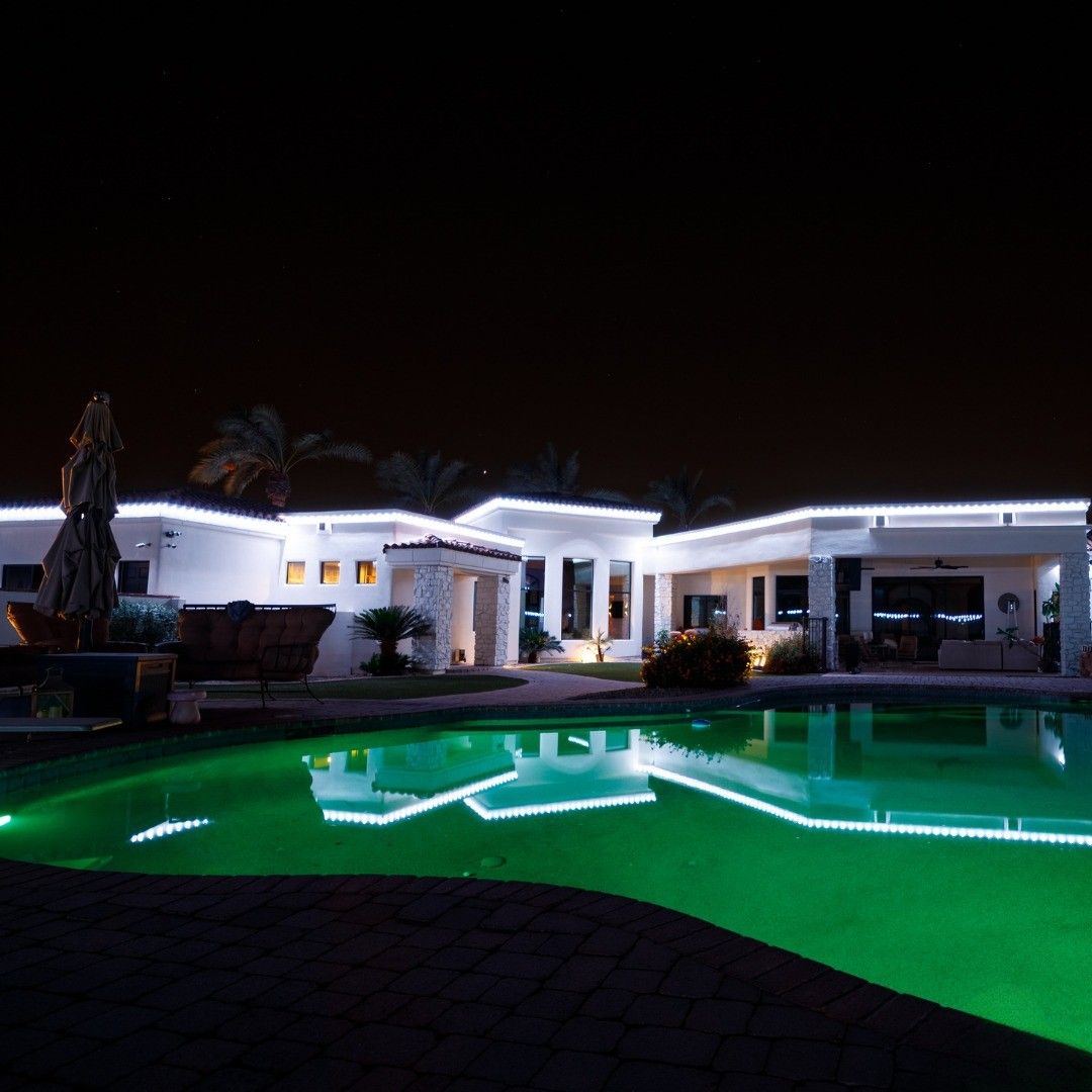 Modern white house at night with a glowing green-lit swimming pool in the foreground