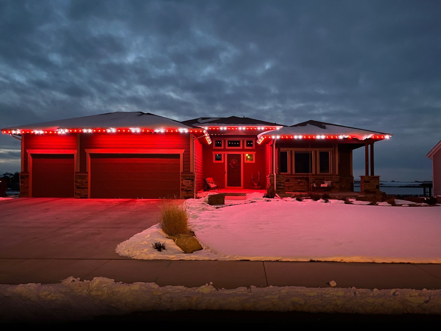 Red-lit house with snow-covered ground at dusk under a dark cloudy sky