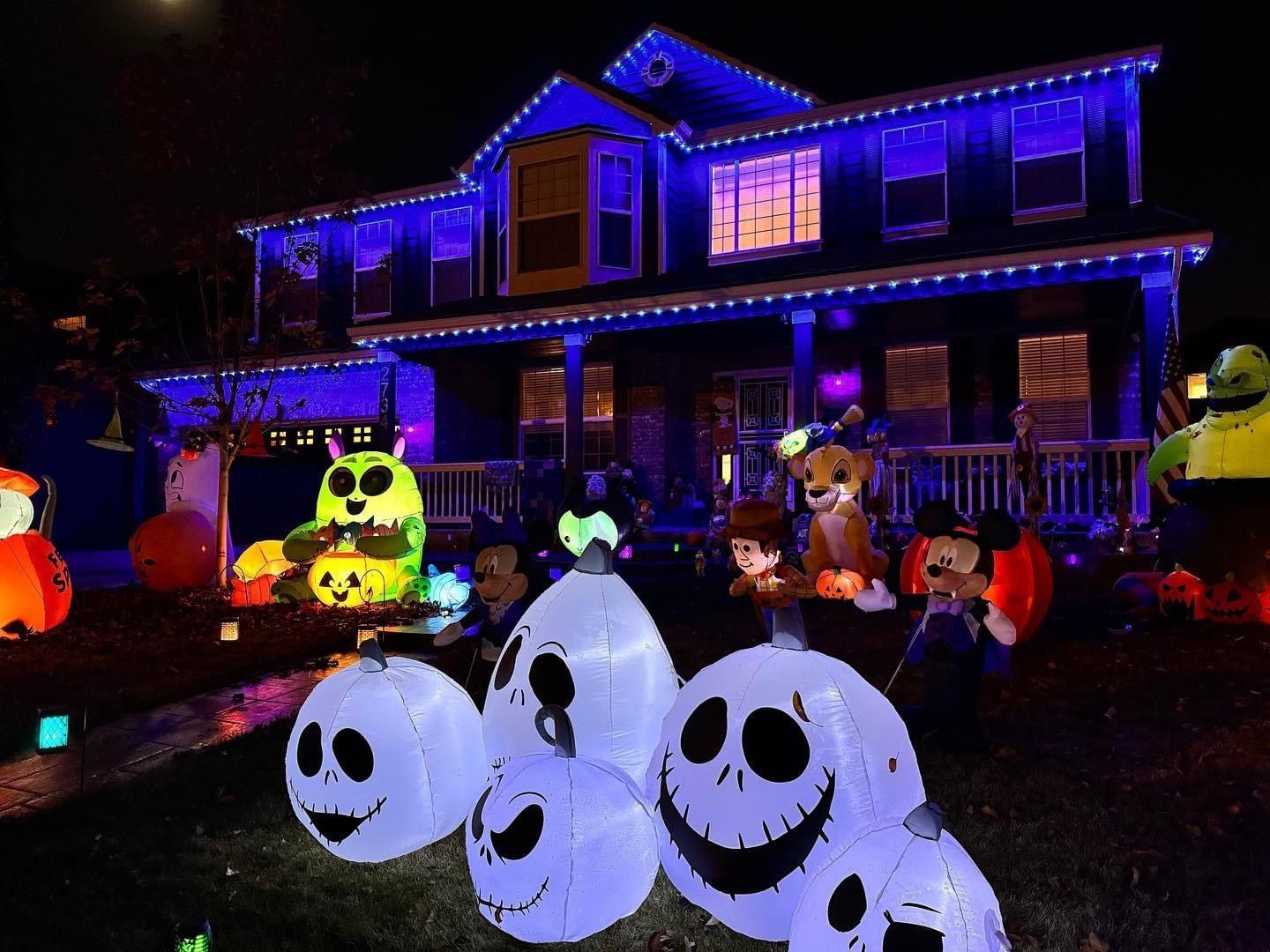 House decorated with blue lights and Halloween lawn displays, including glowing jack-o'-lanterns and ghost figures.