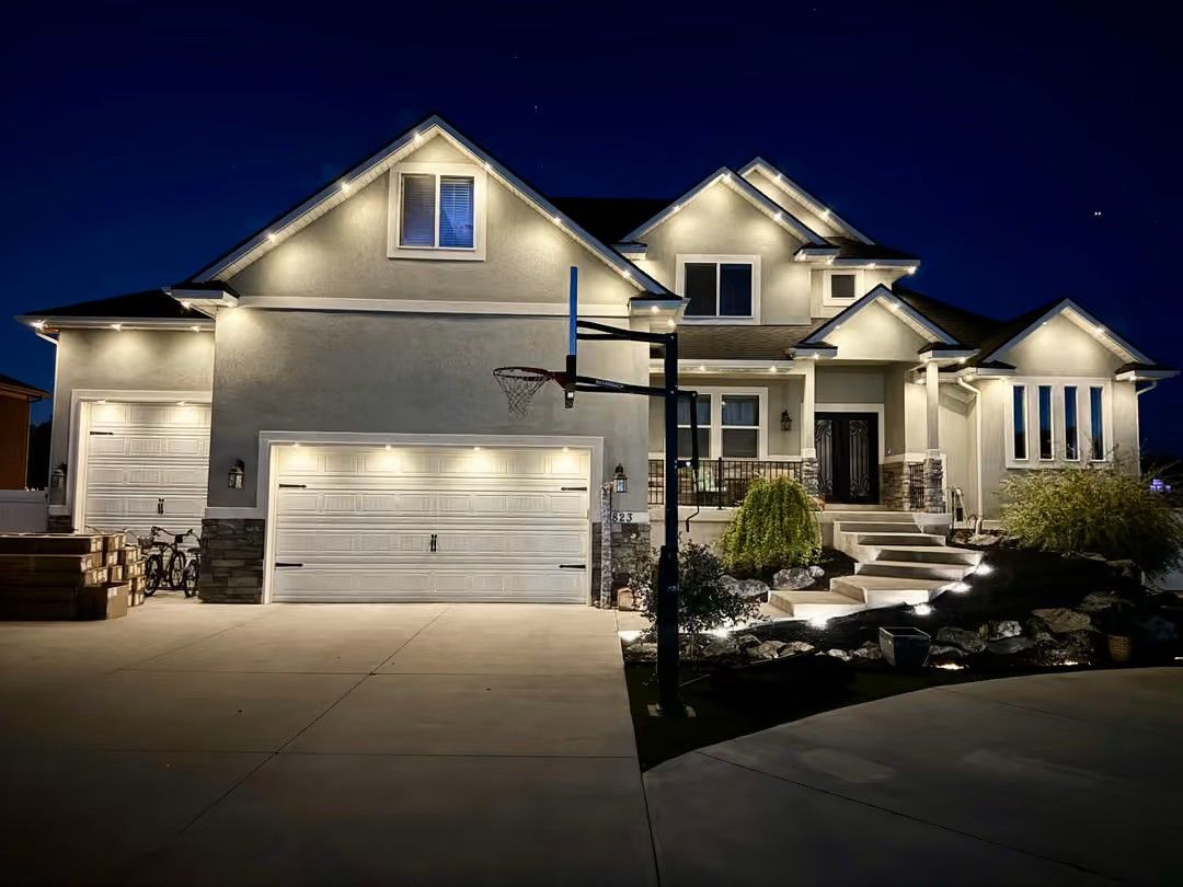 Well-lit suburban house at night with a three-car garage and front steps lit by path lights