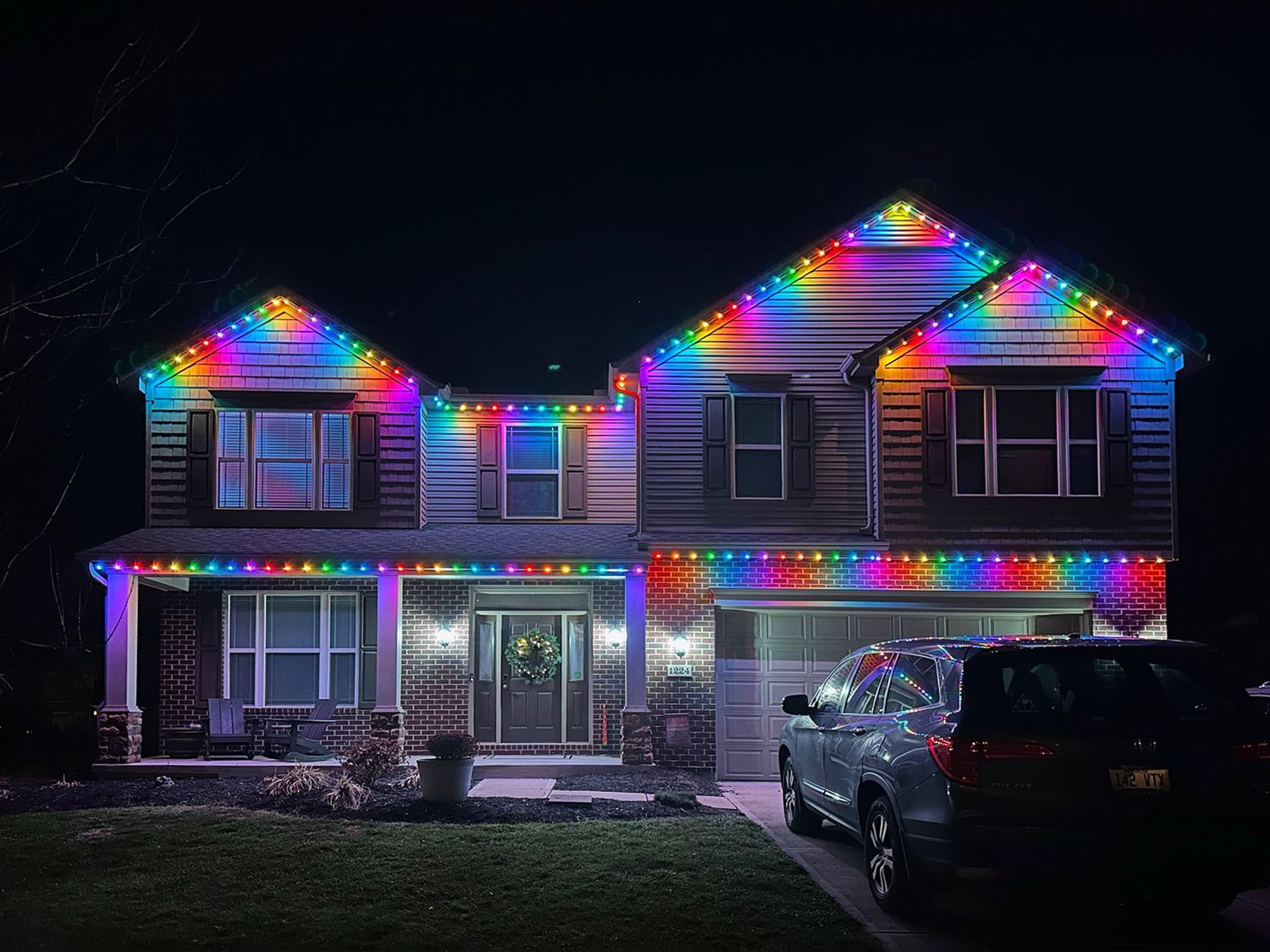 House decorated with colorful Christmas lights at night, with a car parked in the driveway