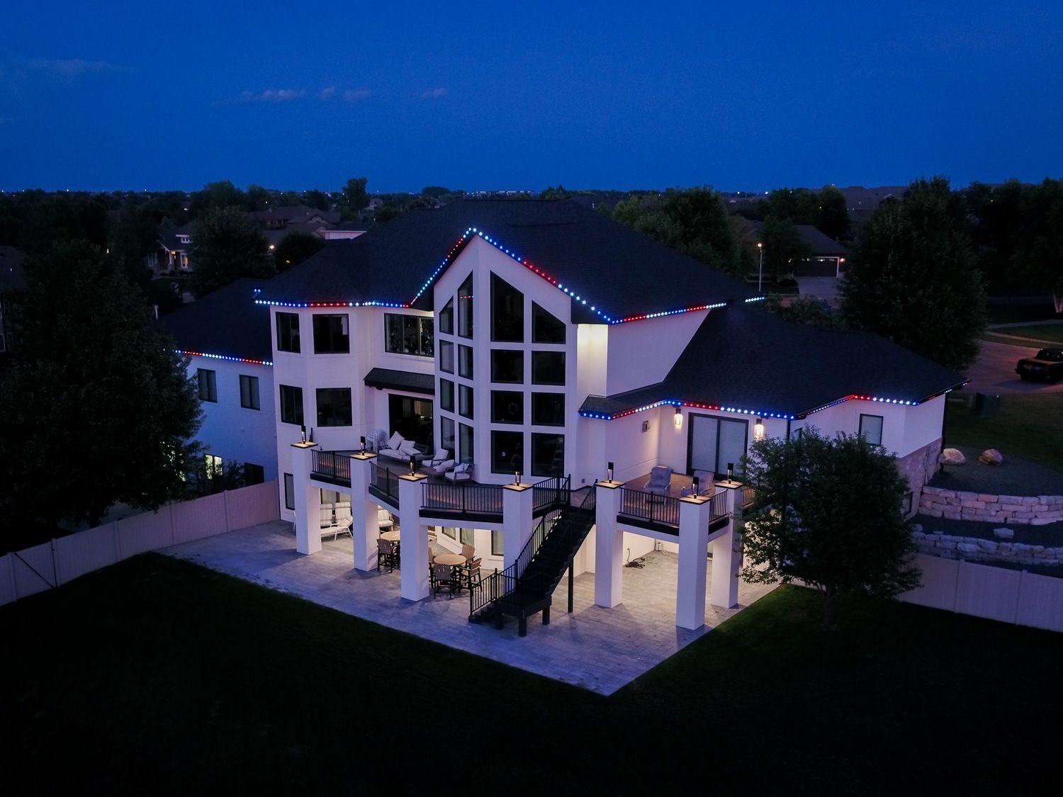 Large white house at dusk with lit windows, string lights, and a courtyard patio.