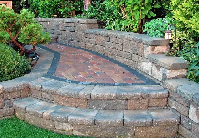 Curved stone garden steps leading to a brick patio beside a retaining wall and greenery