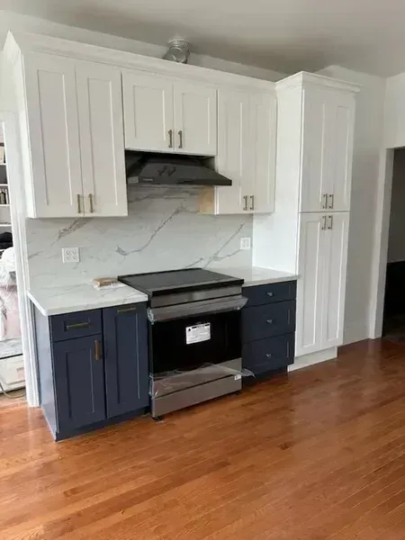 Modern kitchen with white cabinets, navy lower cabinets, stainless stove, and wood floor